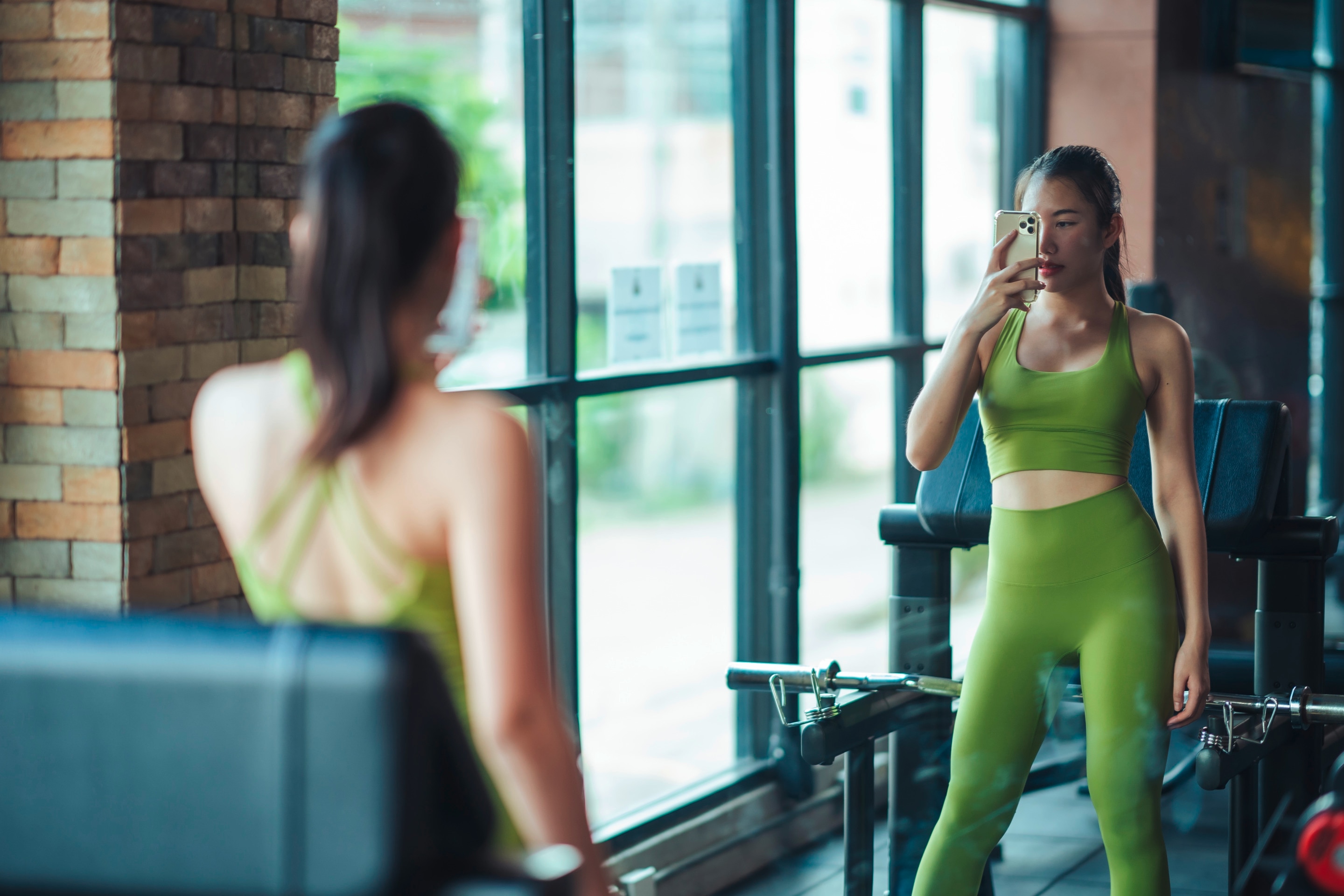 Asian woman taking mirror selfie at the gym.