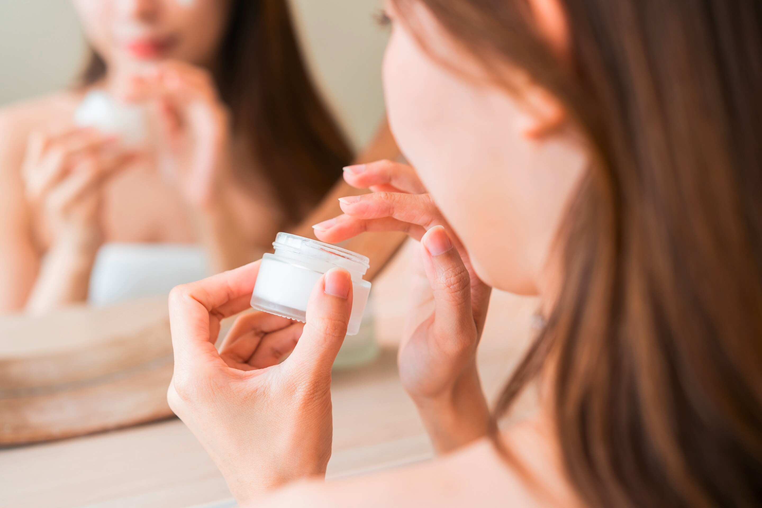 Closeup of woman getting moisturizer from jar. 
