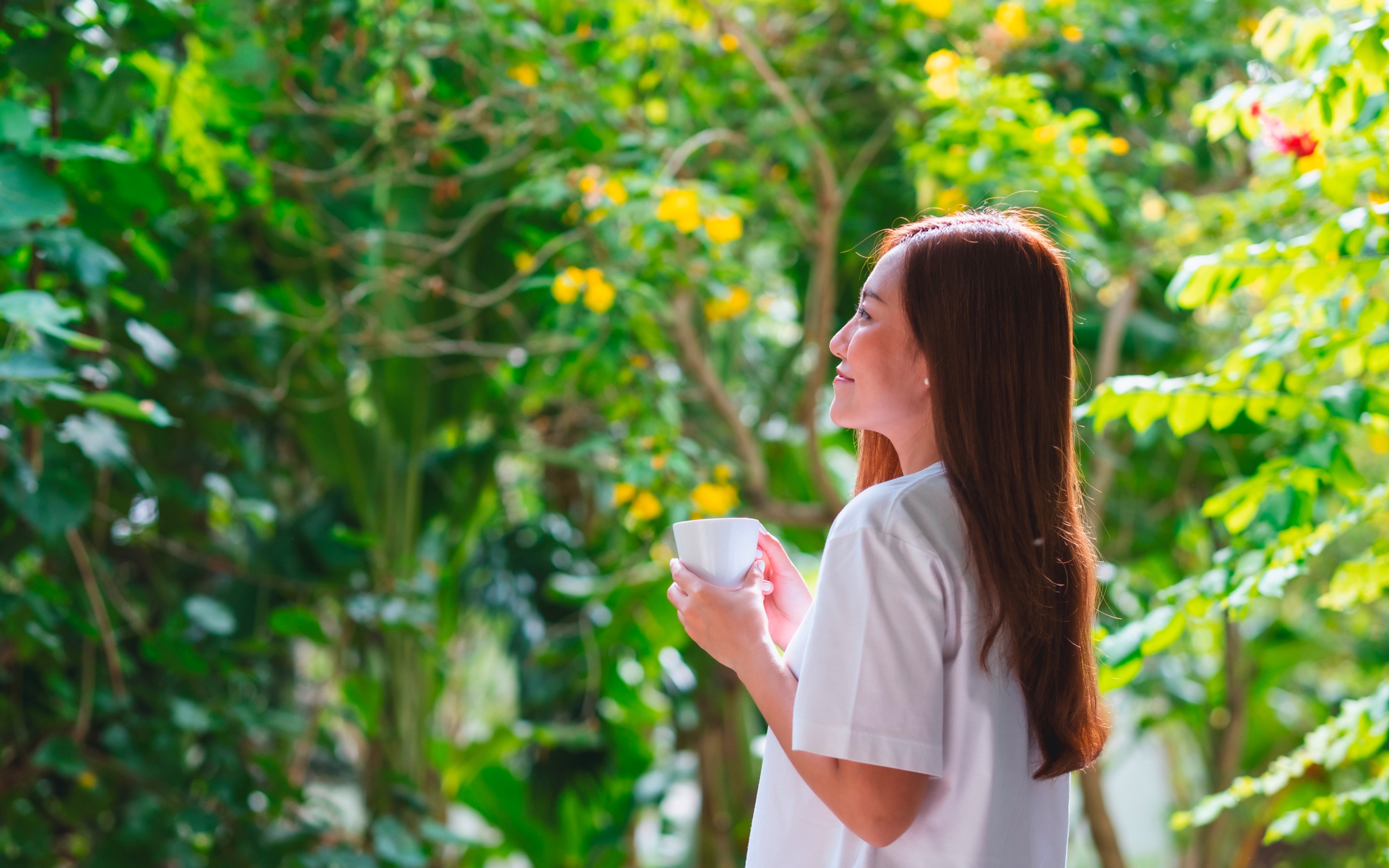 Asian woman holding cup of coffee while looking at nature.