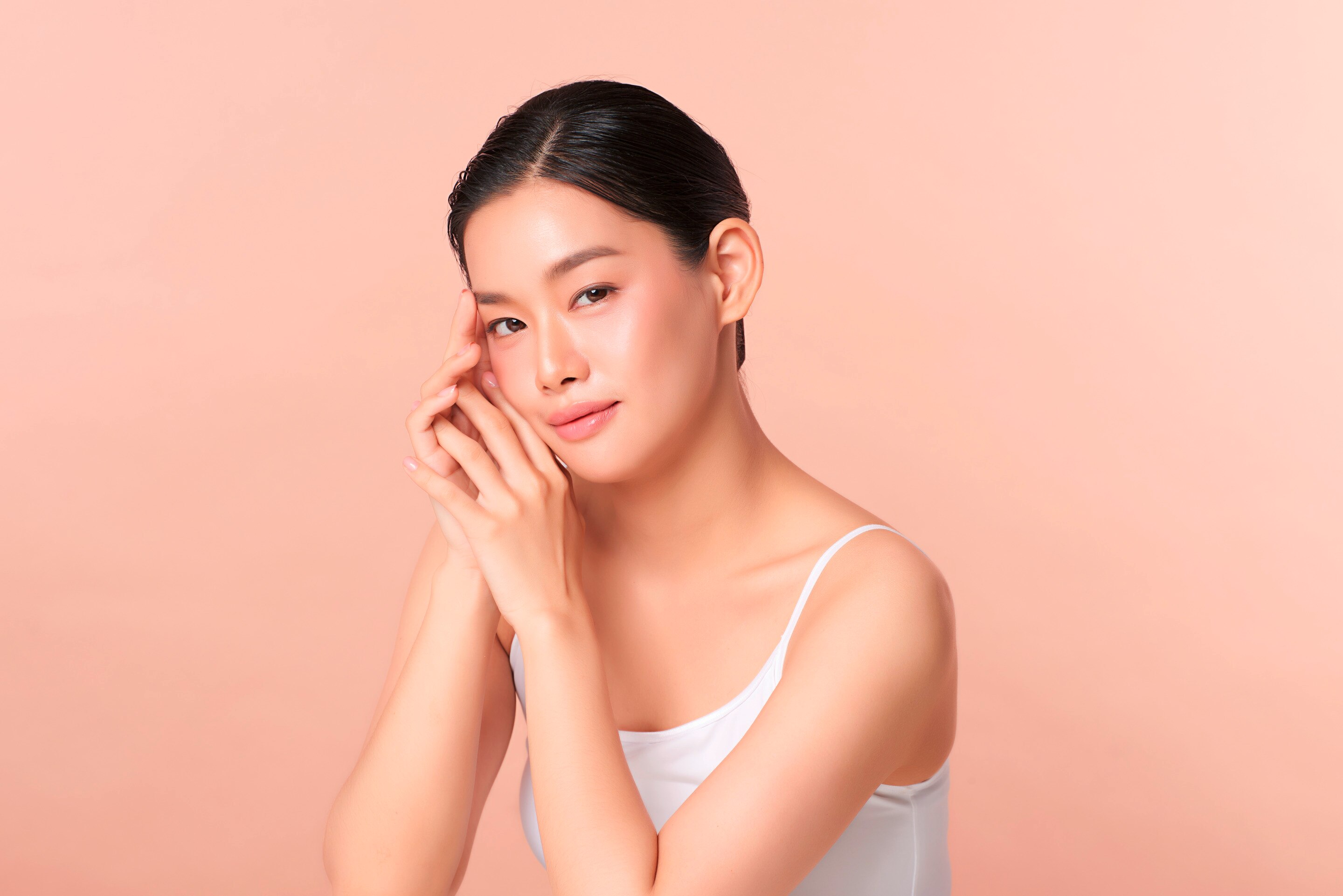 ผู้หญิงเอเชีย รวบผม แสกข้าง สองมือประกบแนบใบหน้า สวมสายเดี่ยวสีขาว