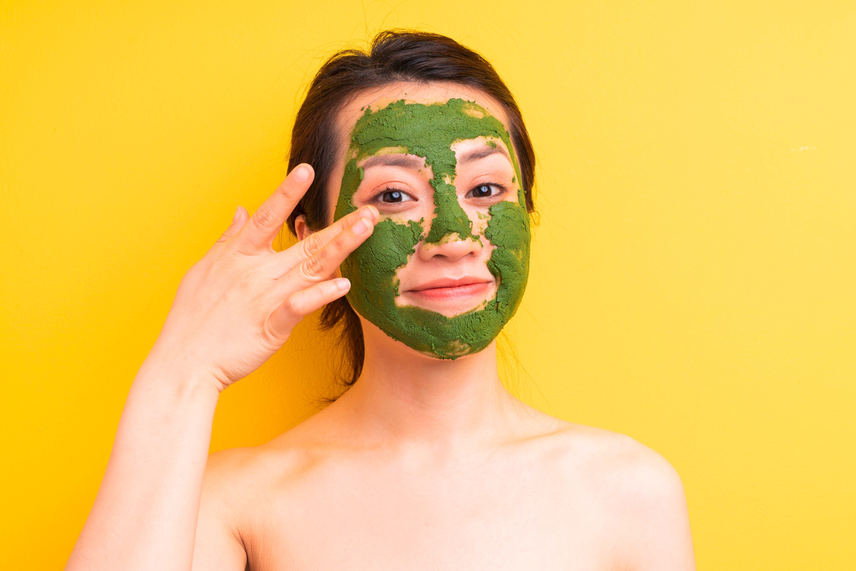 ผู้หญิงเอเชีย รวบผม บนหน้ามีมาส์กสีเขียว มือแตะใต้ตา