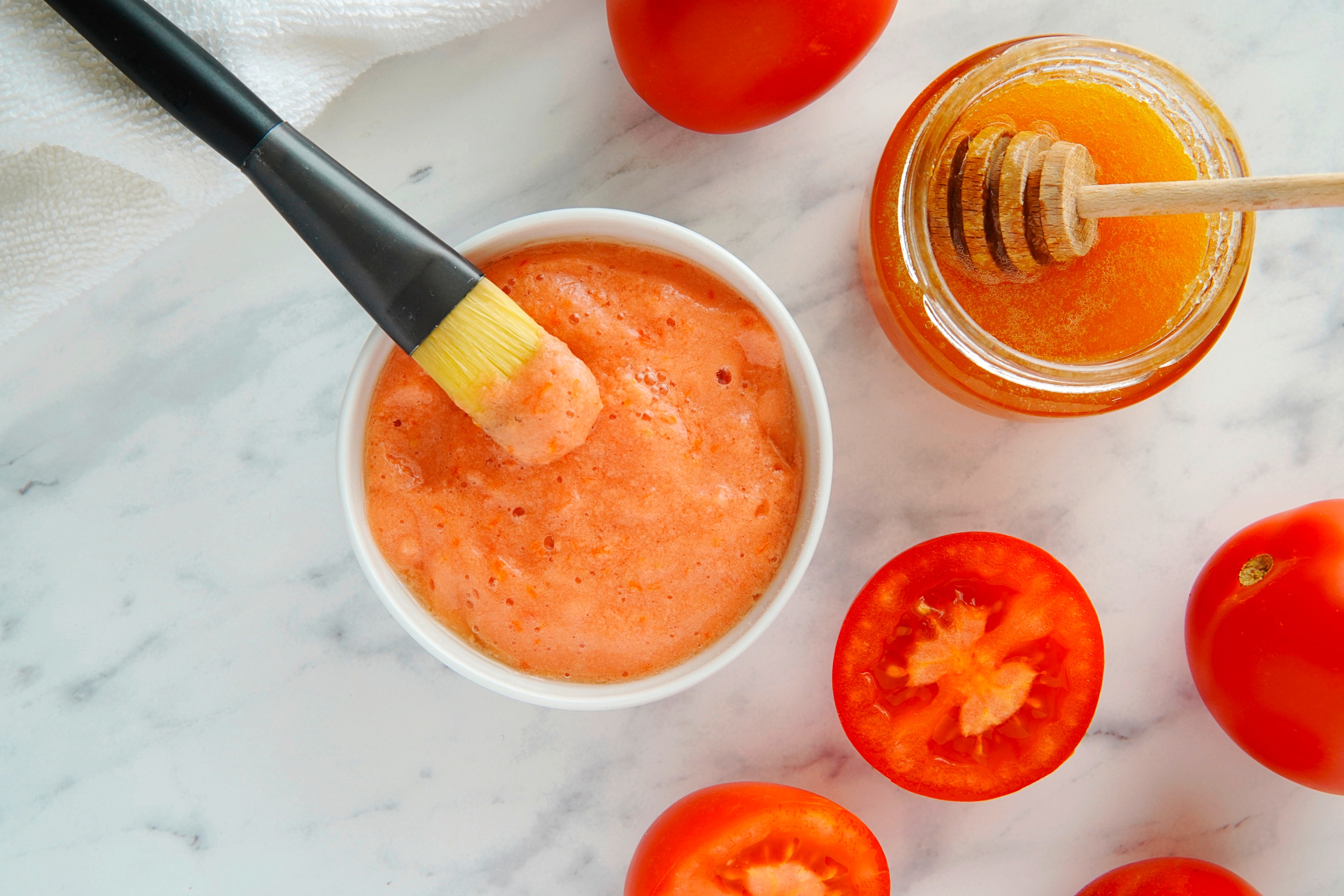 มะเขือเทศผ่าครึ่ง และเต็มผล ถ้วยใส่เนื้อมาส์กและพู่กัน กระปุกใส่น้ำผึ้งและไม้ตัก