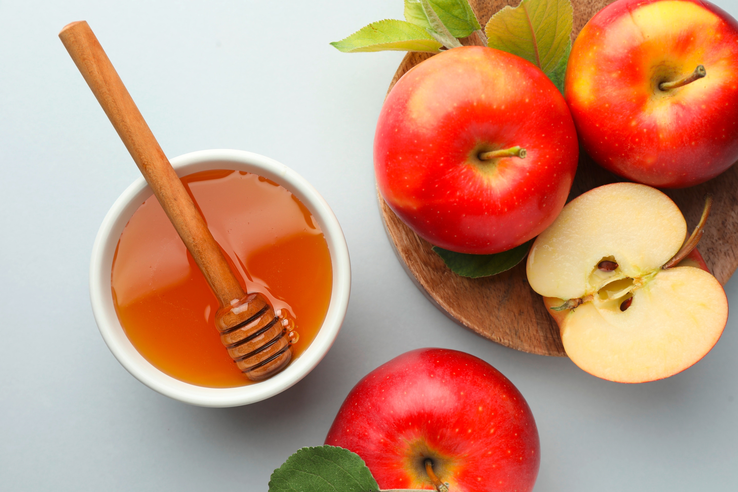 น้ำผึ้งในถ้วยพร้อมไม้ตัก แอปเปิ้ลเต็มลูก แอปเปิ้ลผ่าครึ่ง วางบนจานไม้