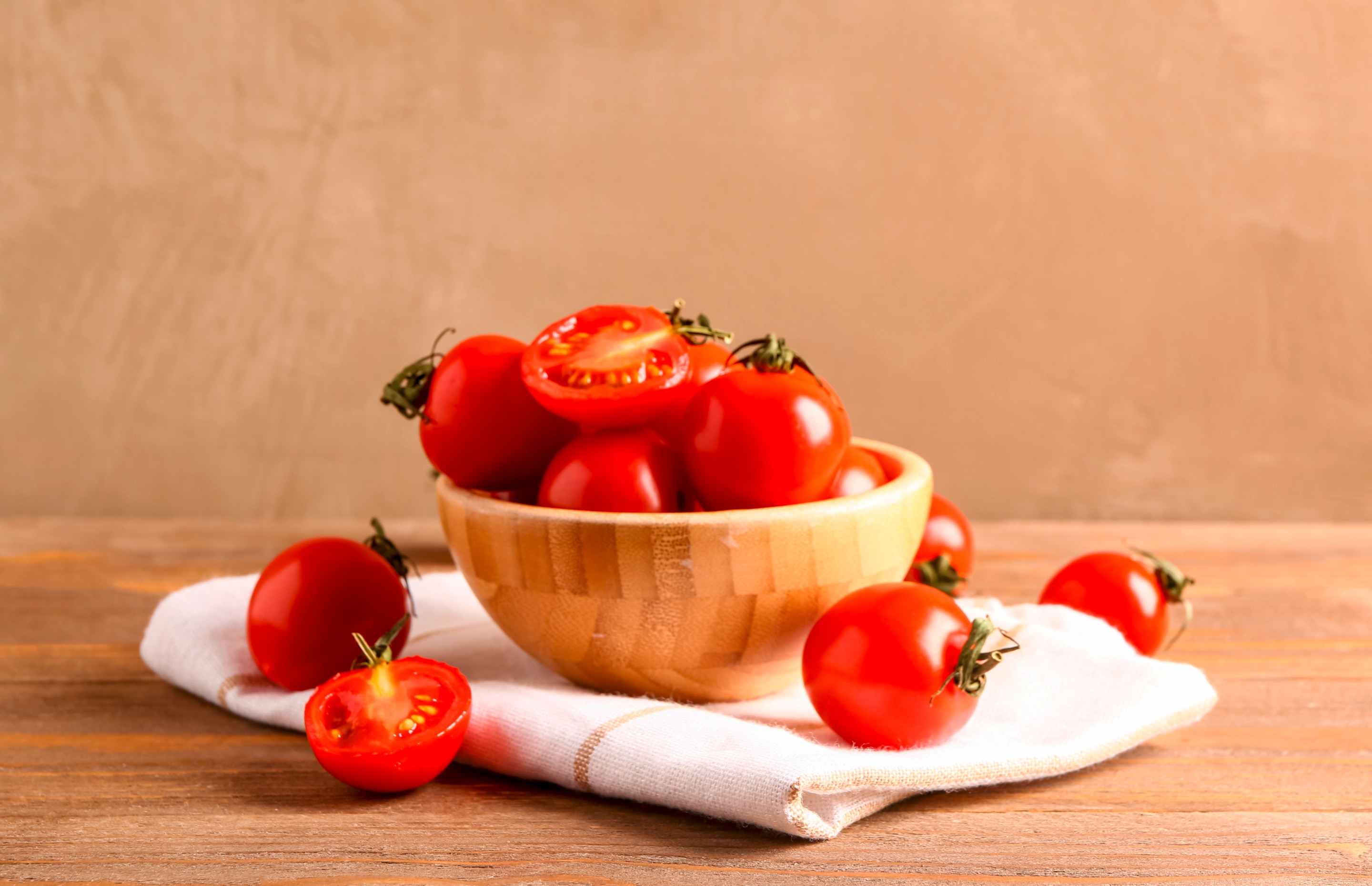 มะเขือเทศสีแดง แบบเต็มผลและผ่าครึ่ง ใส่ในถ้วยไม้ วางบนผ้าสีขาว