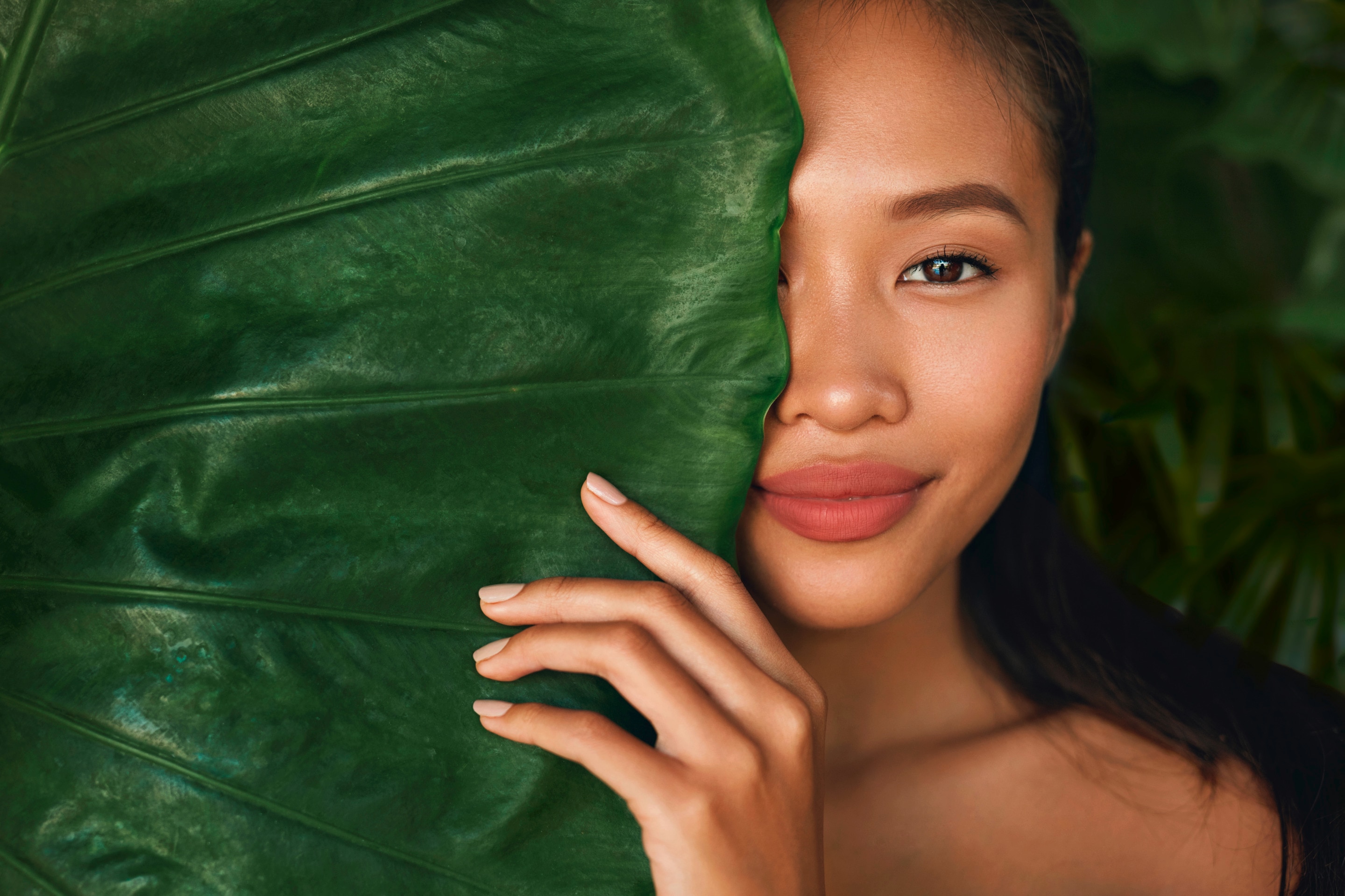 ผู้หญิงเอเชีย รวบผม มือจับใบไม้ ใบไม้ใหญ่บังตาและแก้มเสี้ยวหนึ่ง