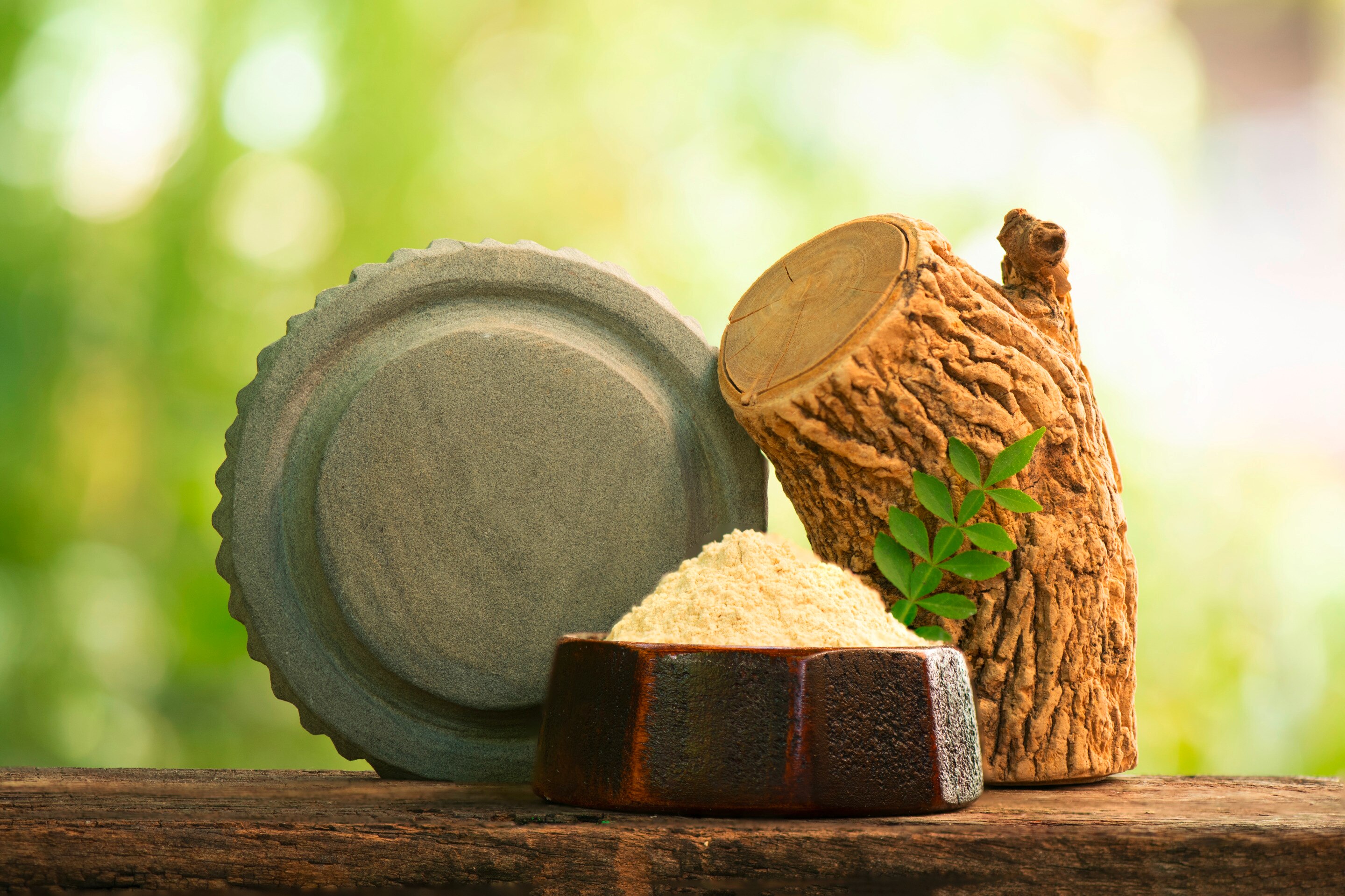 ผงทานาคาในถ้วยดินเผาสีเข้ม ปักกิ่งไม้สีเขียว วางบนแผ่นไม้ ตั้งท่อนทานาคา ไว้ข้างหินฝนทานาคา