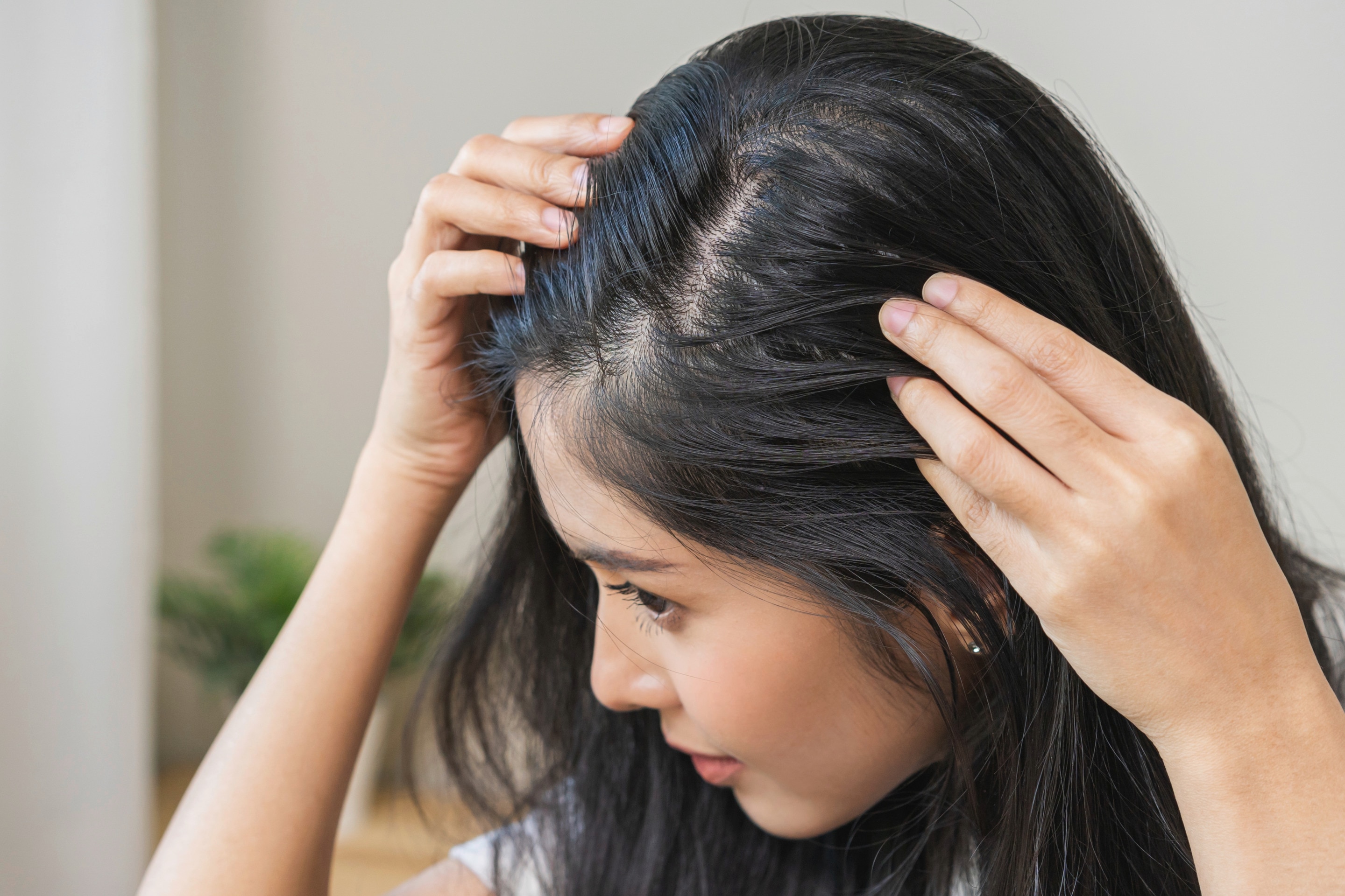 Woman with black hair checking scalp.