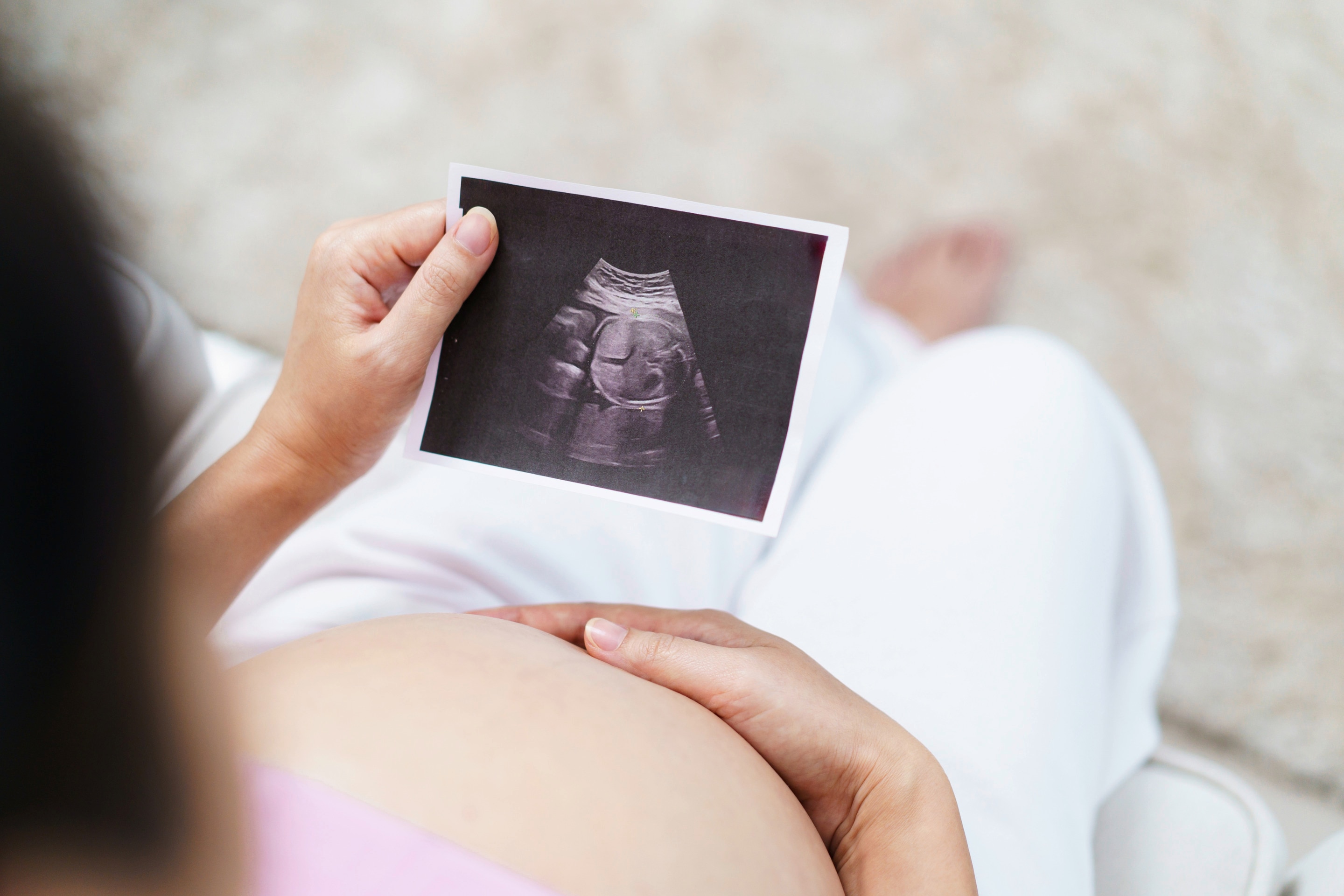 seorang ibu hamil memegang foto hasil USG janin sambil menyentuh perutnya pada usia kehamilan 8 bulan.