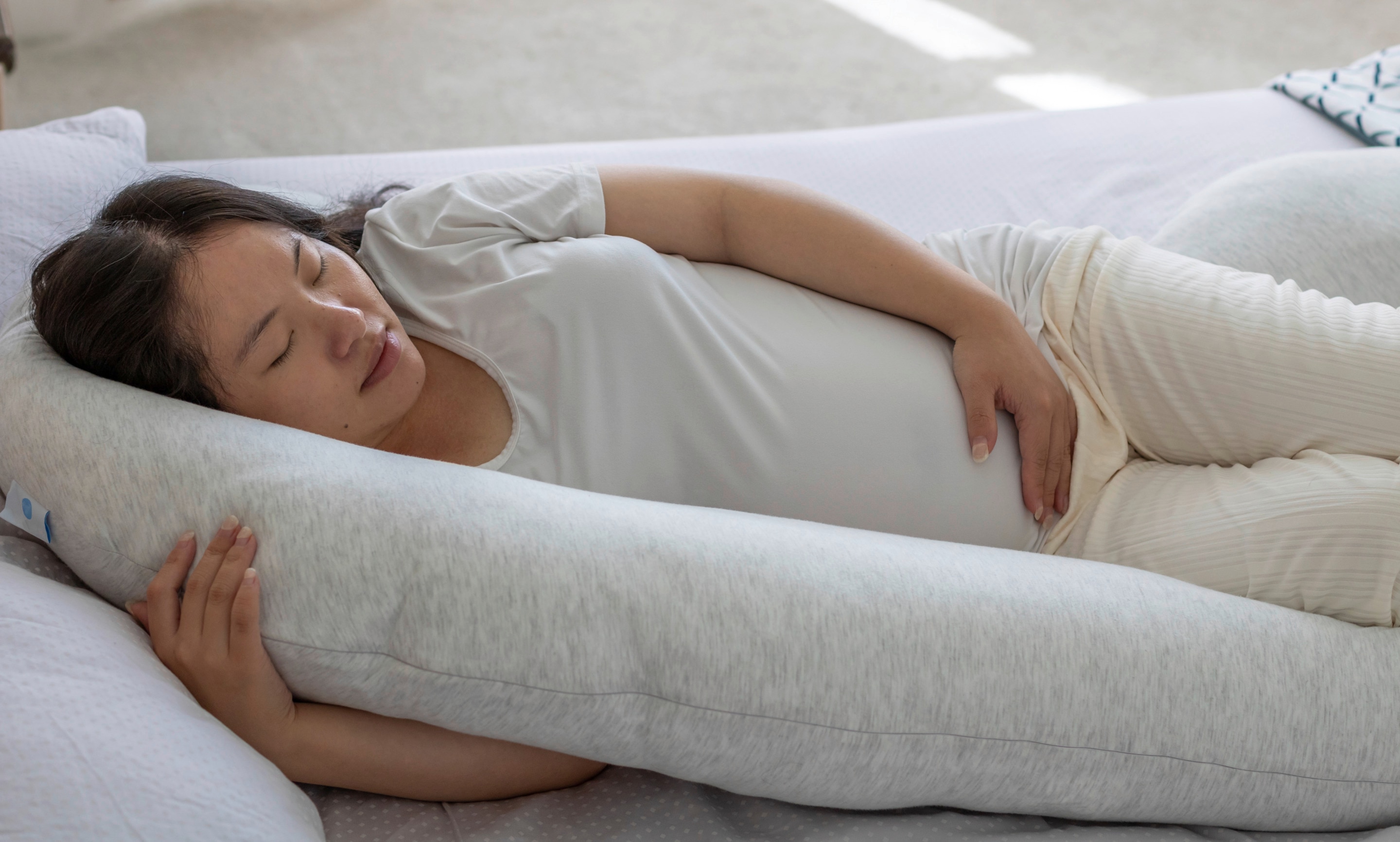 Ibu hamil sedang berbaring dengan posisi tidur miring ke kiri menggunakan bantal tambahan
