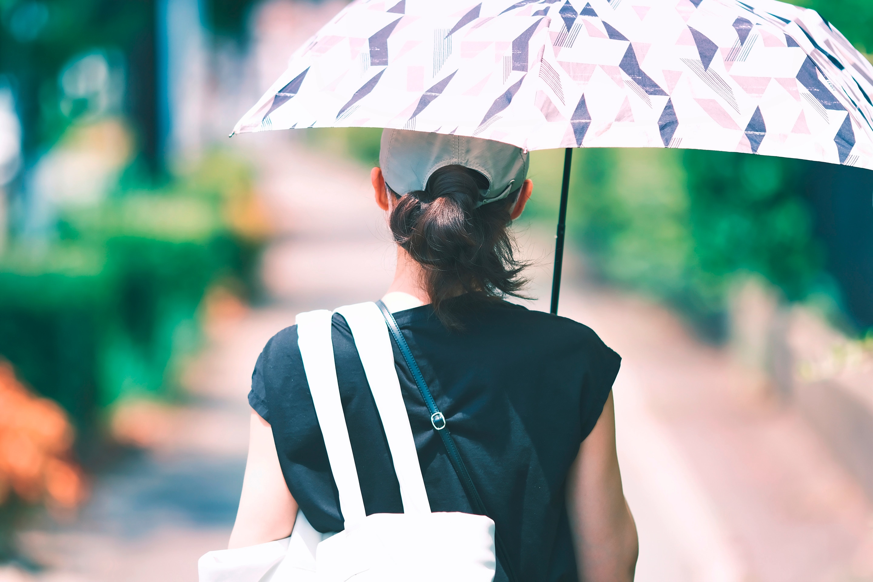 Back of woman wearing hat and holding umbrella while walking outdoors.