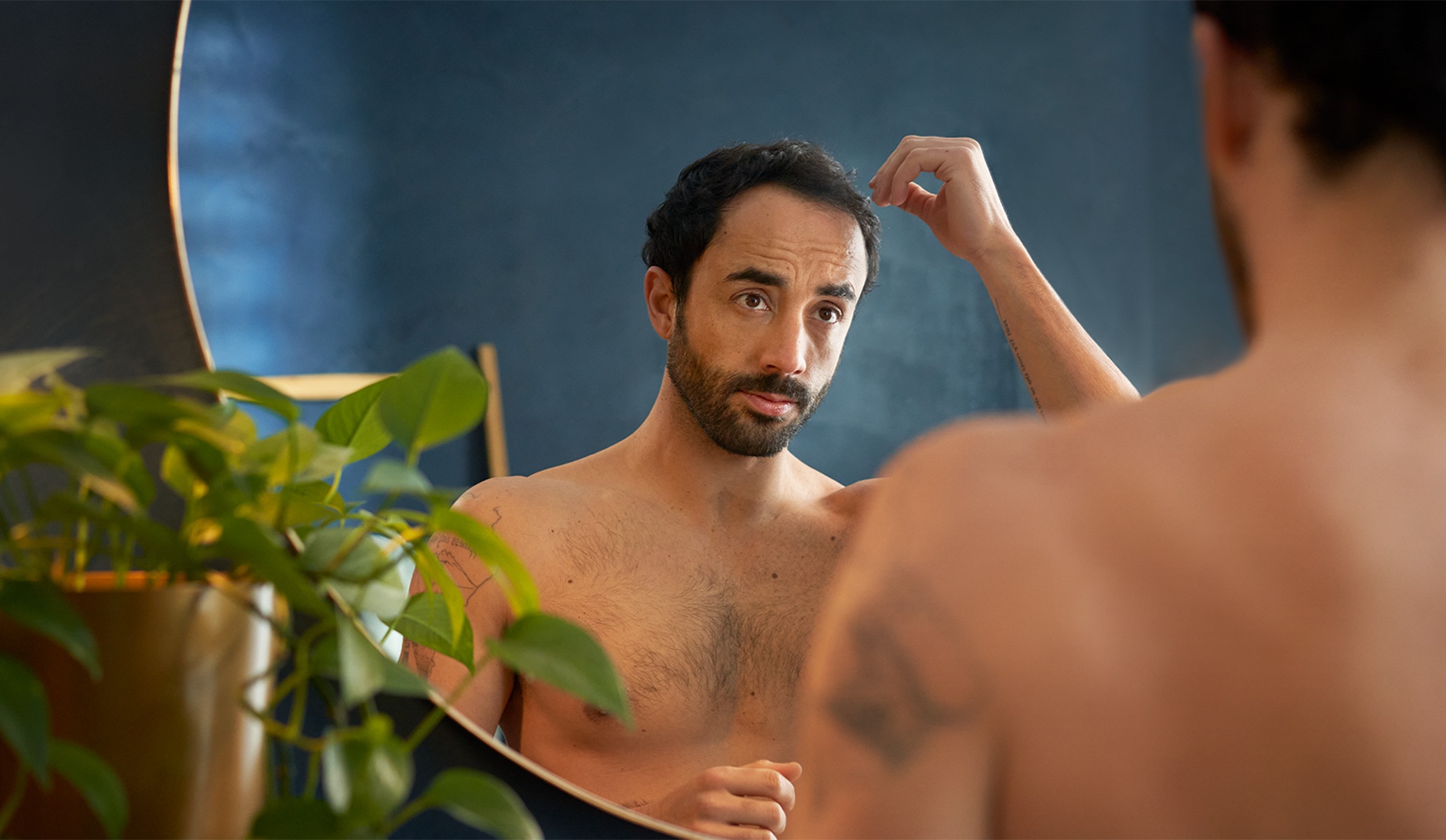 Man looking in the mirror holding a hair strand