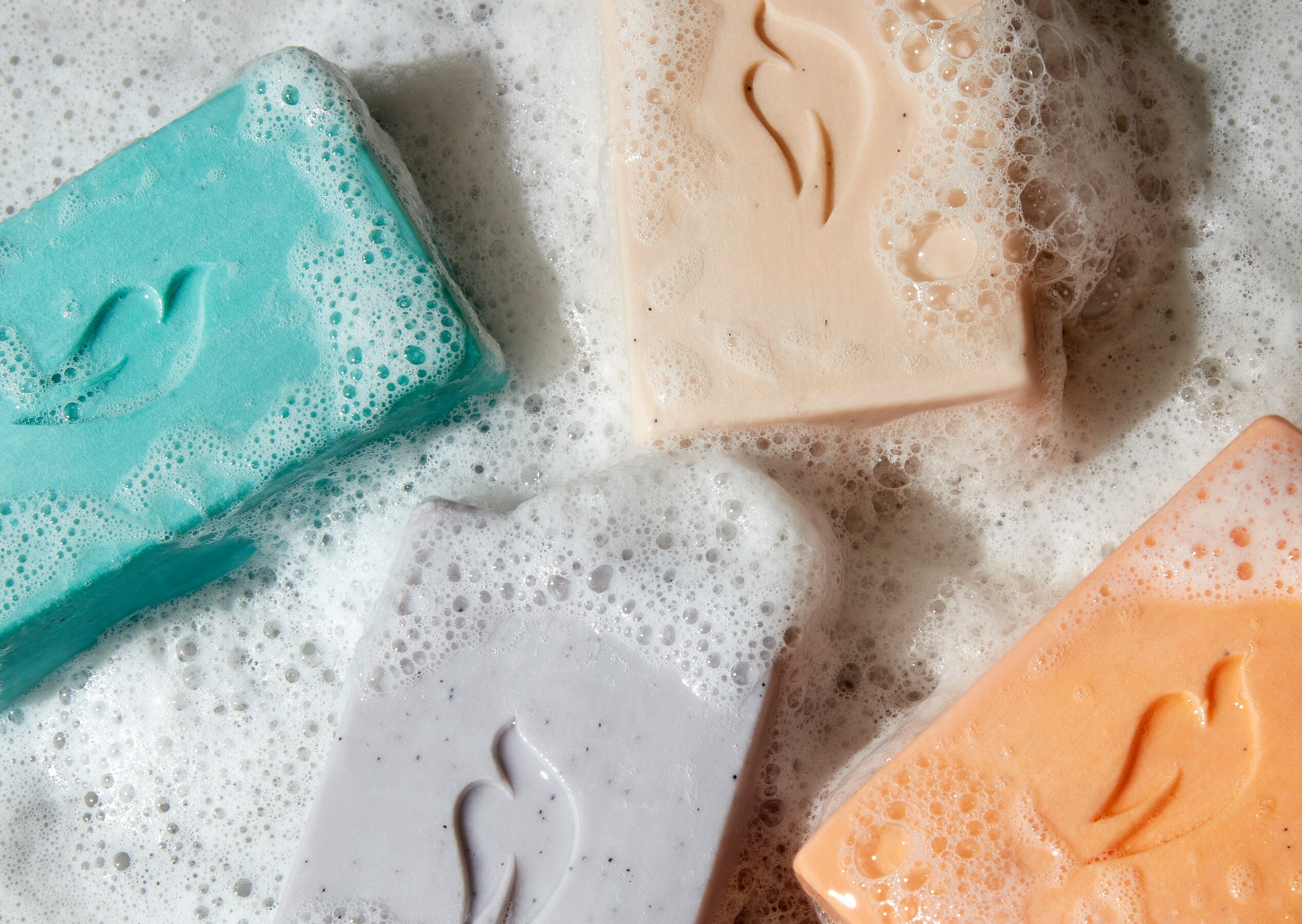 Collection of five colorful Dove Men+Care cleansing bars lying on a bathroom surface, lathered with foam