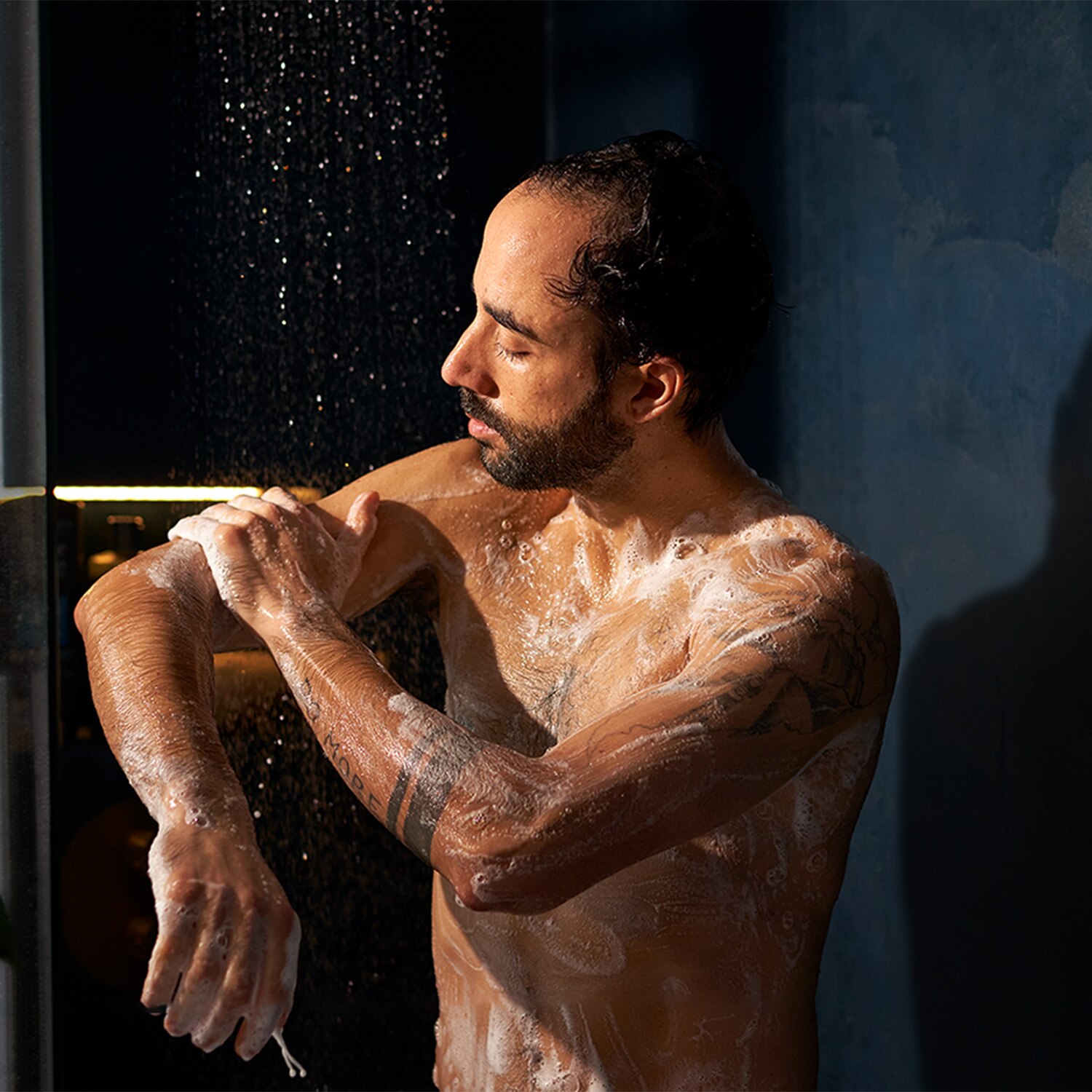 Man in the shower, rubbing Dove Men+Care body wash product into his arm