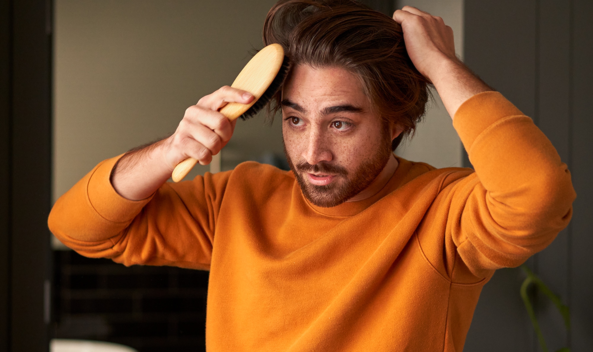 Man in an orange sweater brushing his hair
