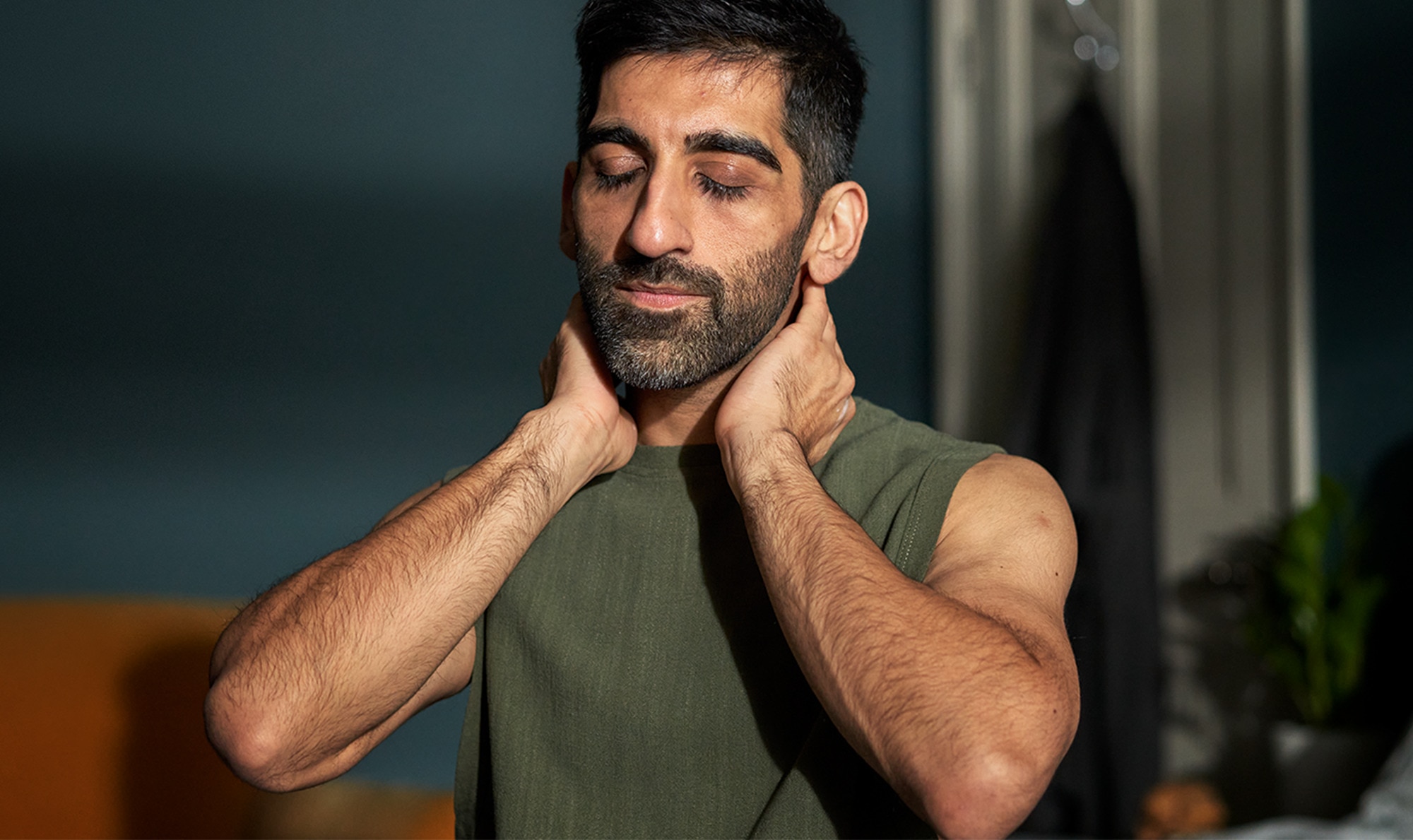 Man with eyes closed and hands coupled around his neck in his bedroom