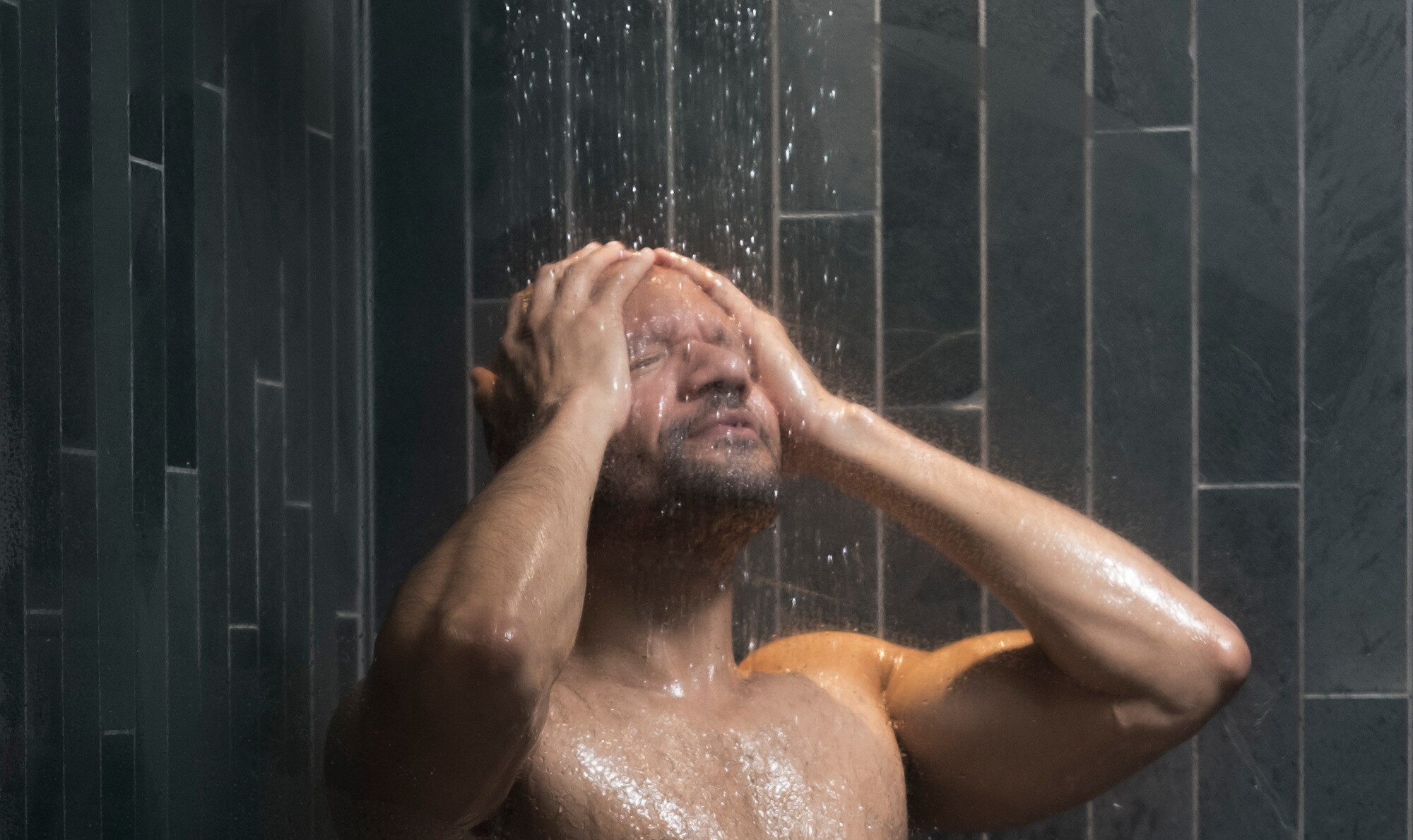 Man standing under the shower with head tilted up, rinsing his face