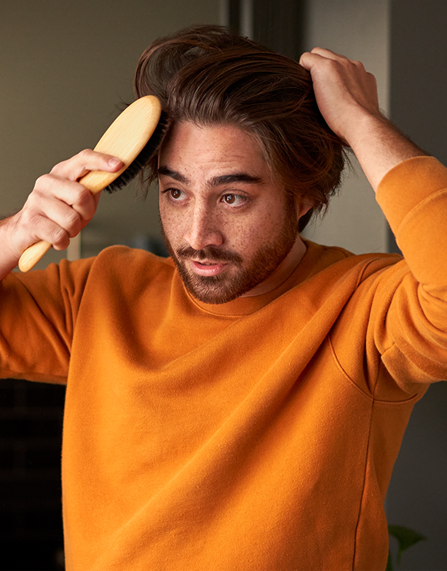 Man in an orange sweater brushing his hair
