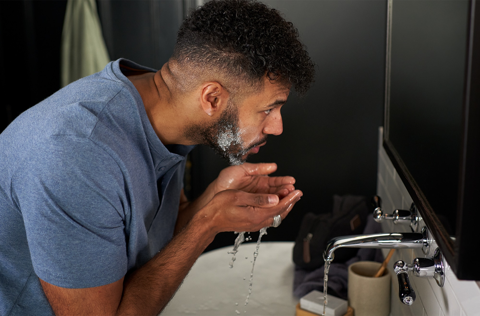 Man looking in the mirror and rinsing shaving foam from his beard over a basin