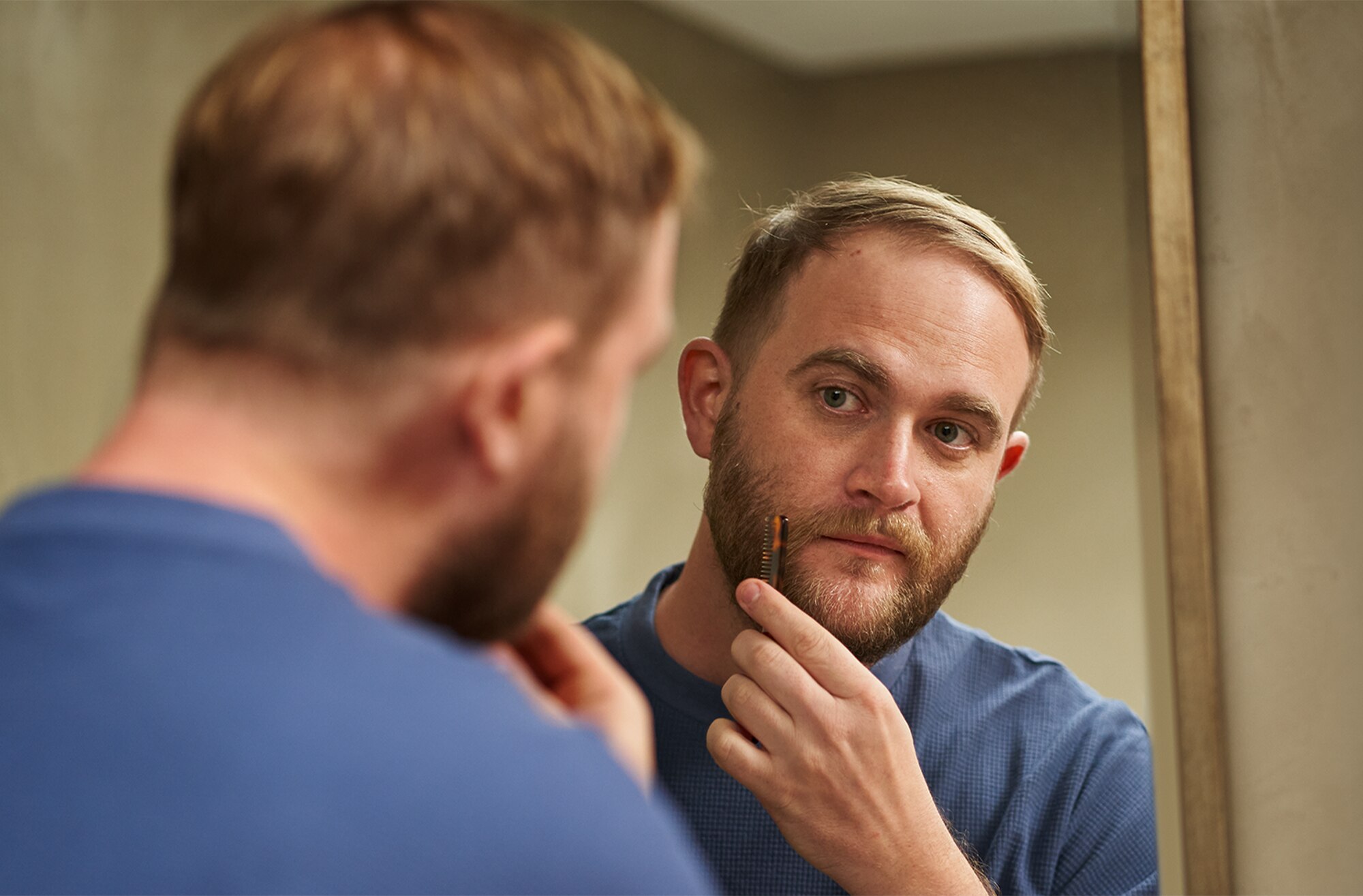 Man looking in the mirror and combing his beard