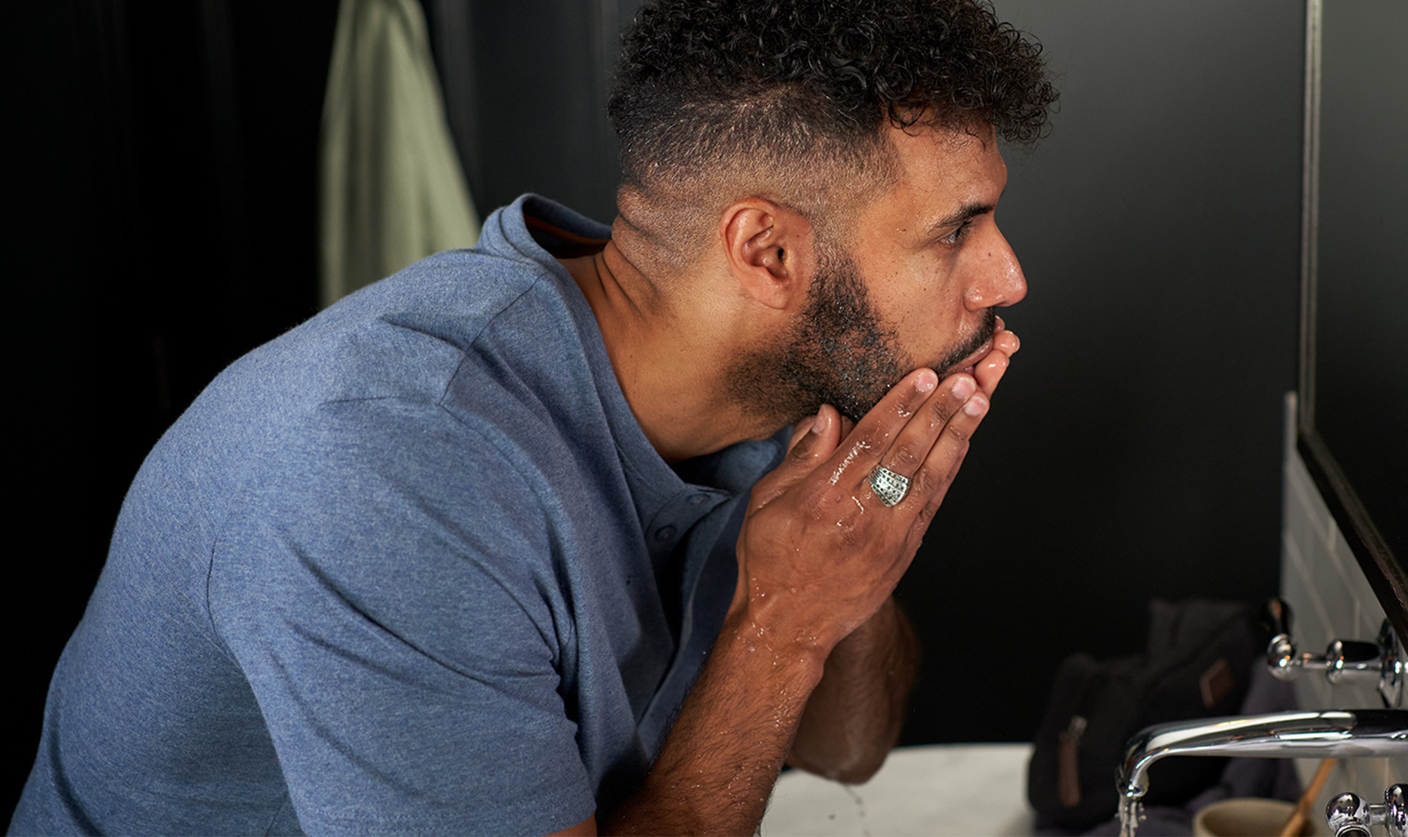Image of a man looking in the mirror and rinsing shaving foam from his beard over a basin