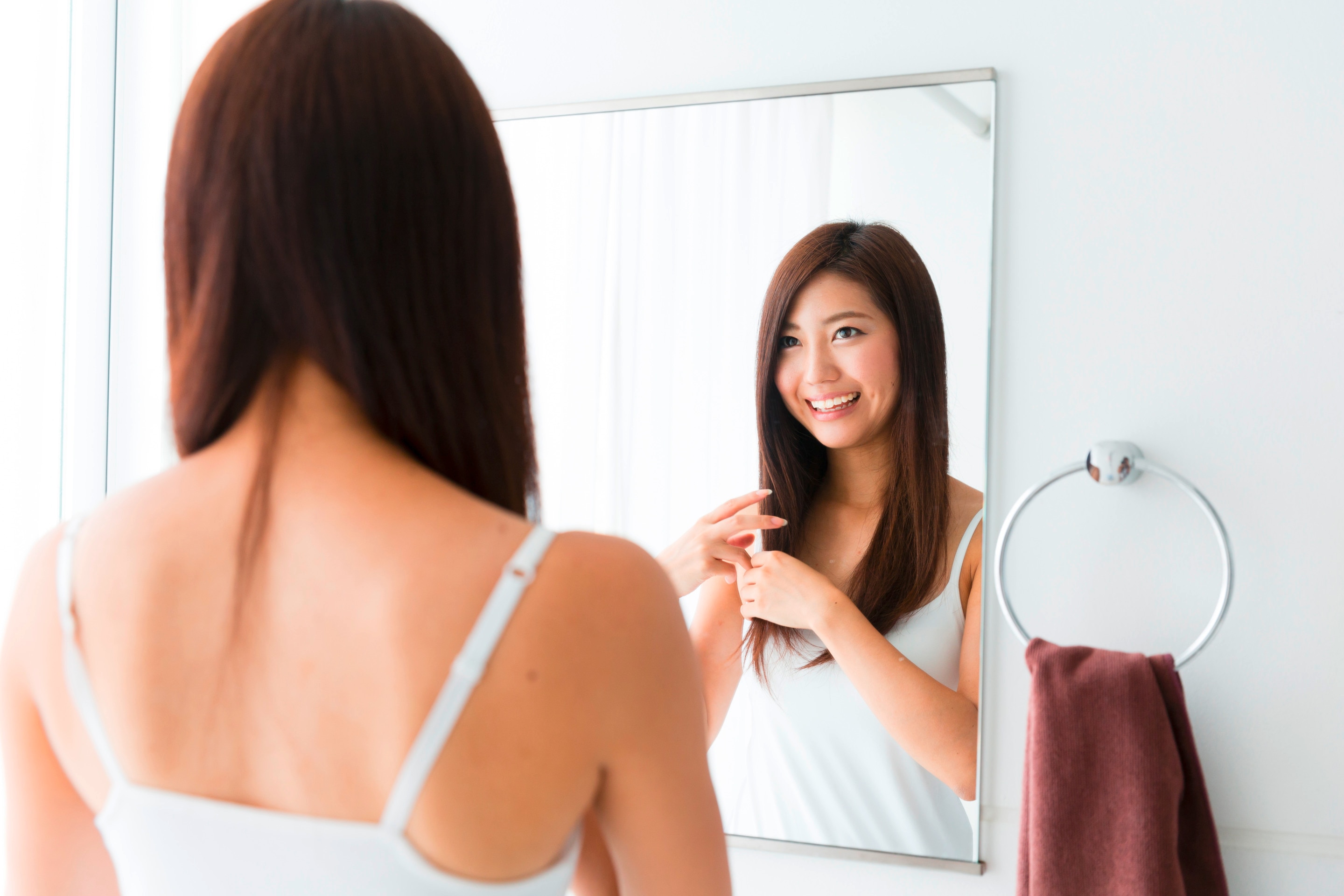Smiling woman applying cream to her hair in the bathroom.