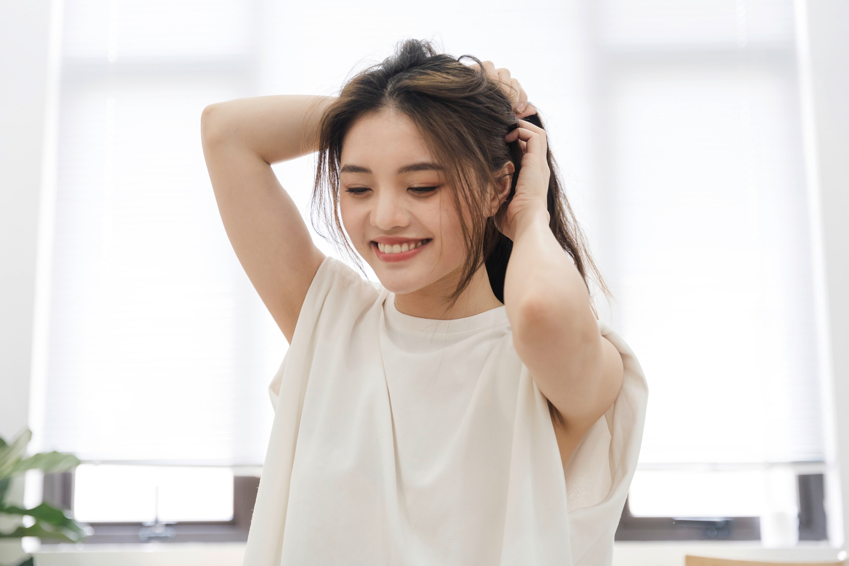 Woman tying her long layered hair into a ponytail.