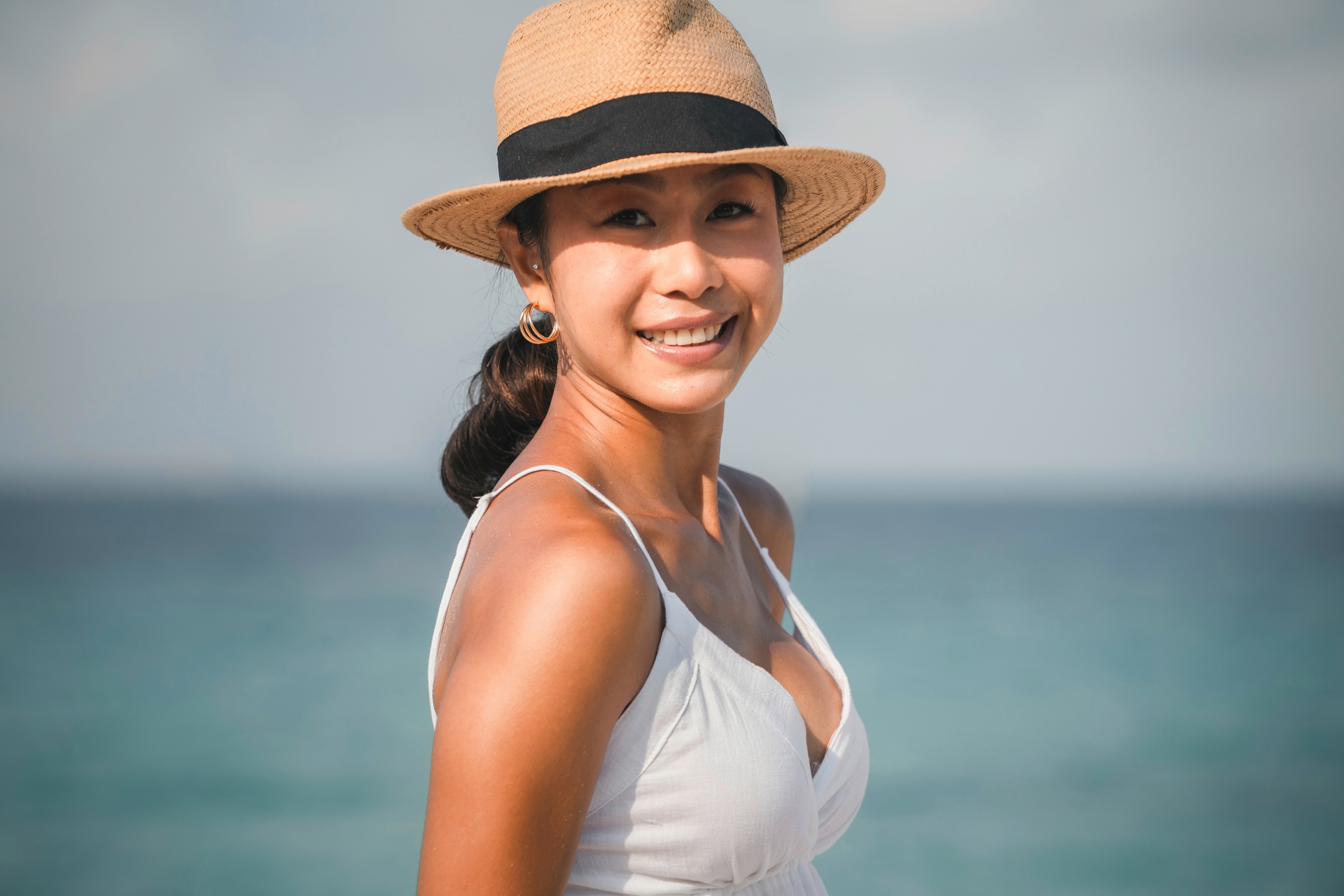Woman wearing a straw hat standing at the beach.
