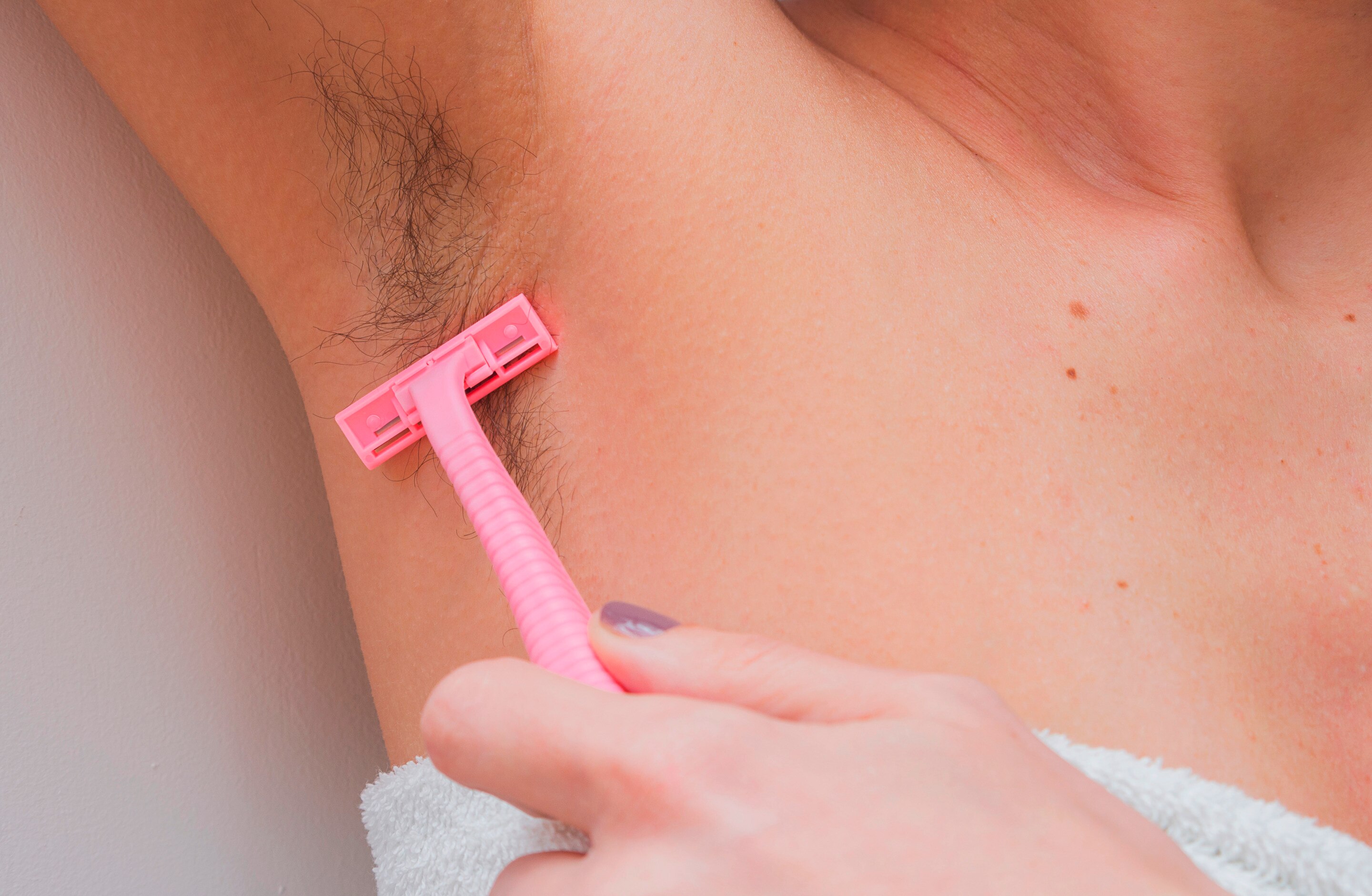 Closeup of woman shaving long armpit hair.