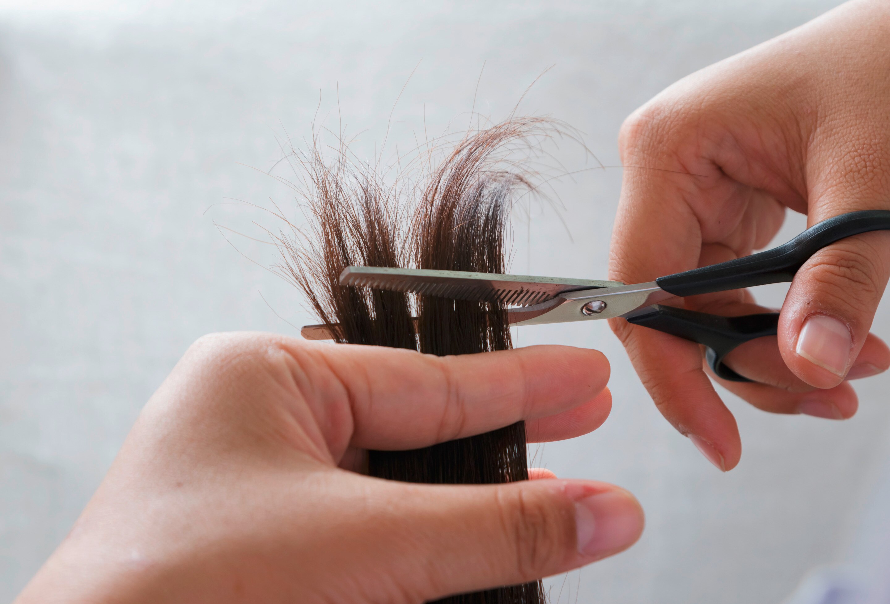 Closeup of hands trimming ends of hair with scissors.