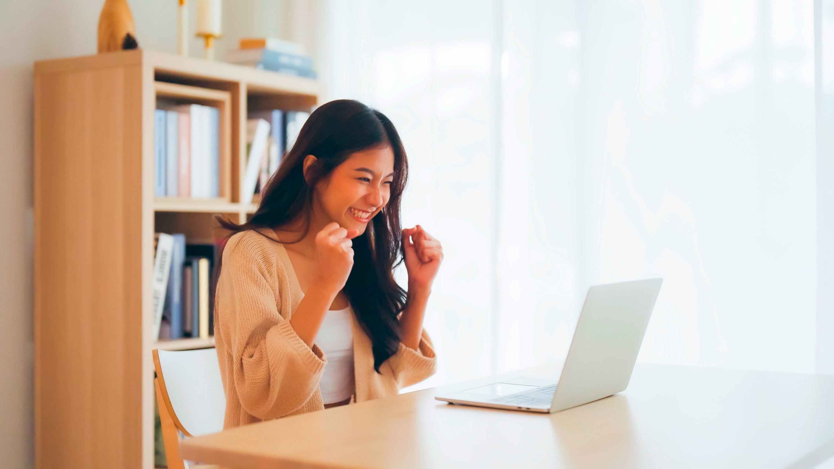 Happy Asian woman cheering in front of laptop.