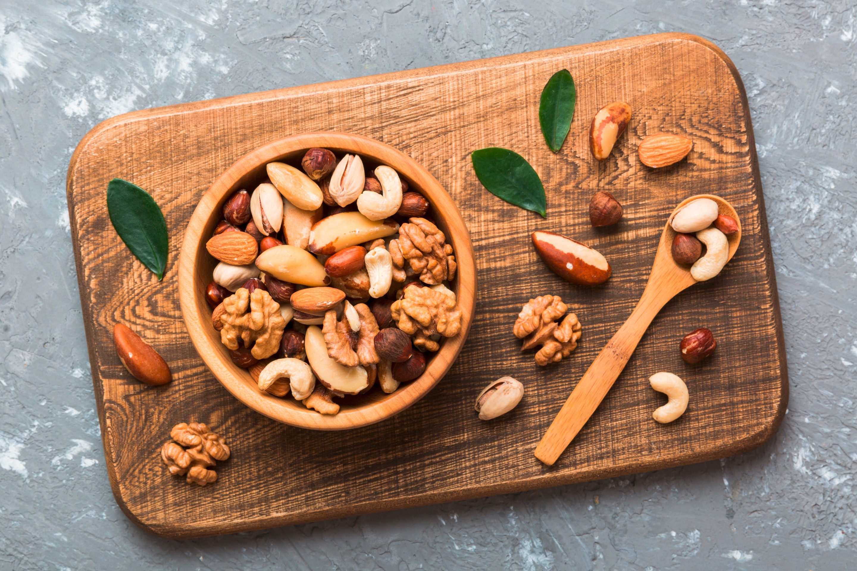 เมล็ดถั่วหลายชนิดในถ้วยไม้ และช้อนไม้ ใบไม้สีเขียว วางบนเขียงไม้