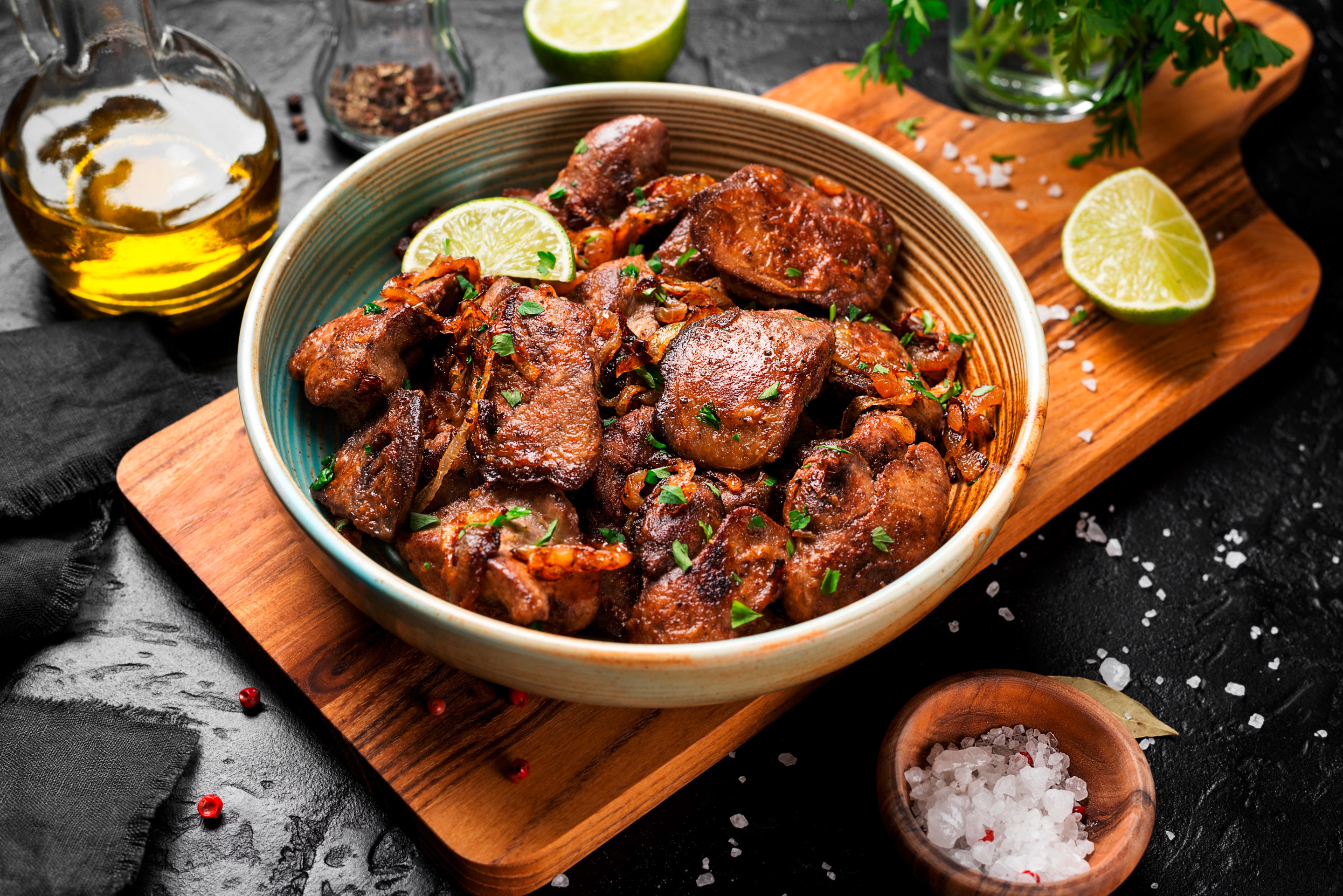 ตับไก่ผัด มะนาวผ่าซีก เขียงไม้ เม็ดเกลือในถ้วยไม้และโรยบนพื้น ขวดน้ำมันมะกอก