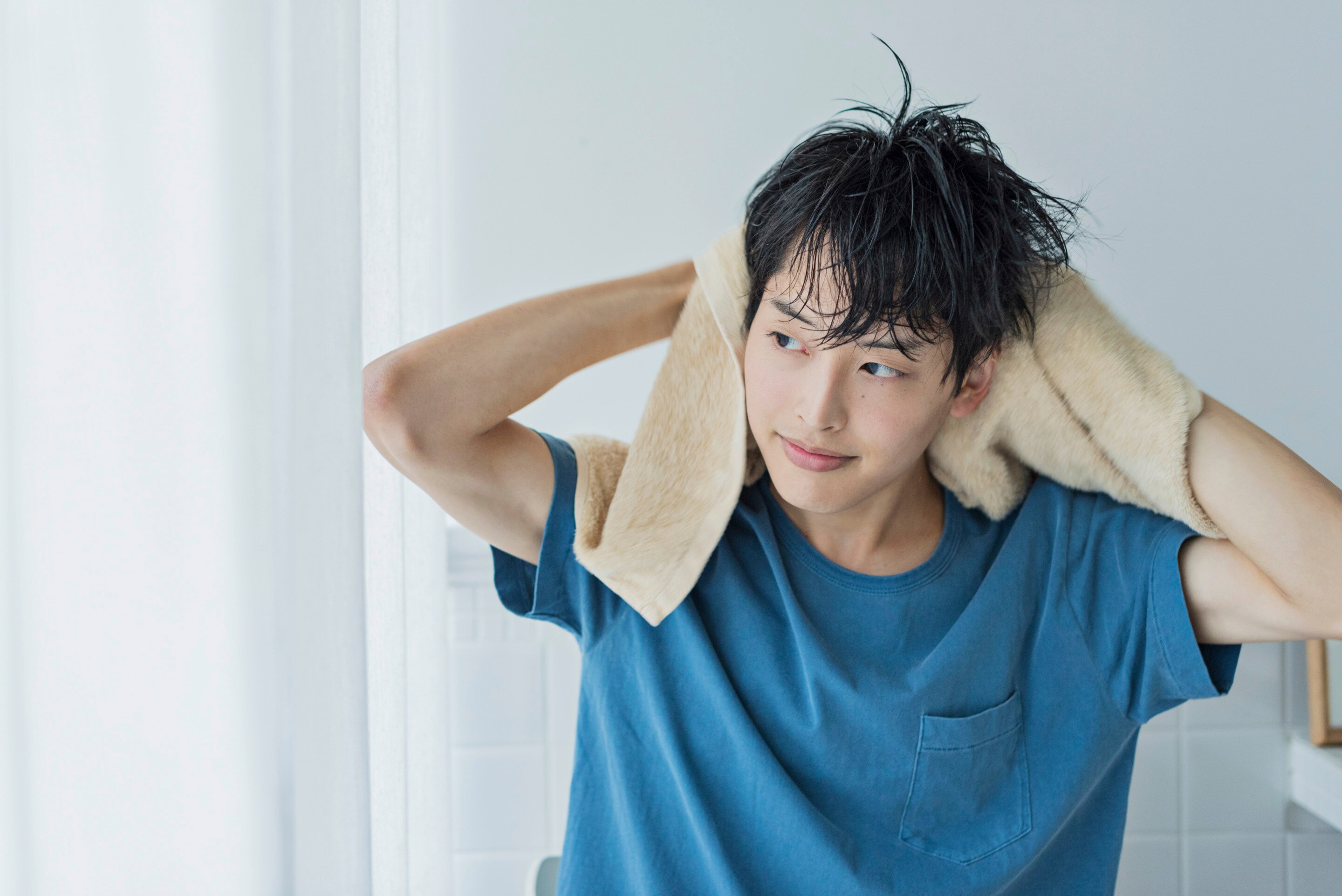 ผู้ชายเอเชีย ผมเปียกหมาด ใช้ผ้าขนหนูสีน้ำตาลเช็ดผม ใส่เสื้อสีฟ้า อยู่ในห้องน้ำ