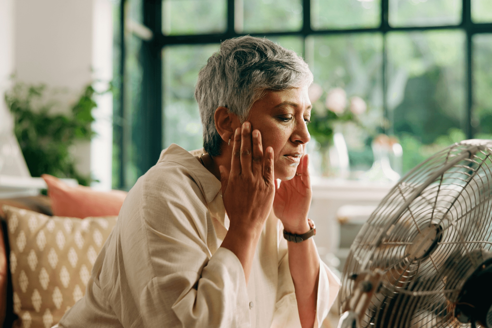 Woman sitting in front of fan trying to cool down and reduce sweat caused by her medication