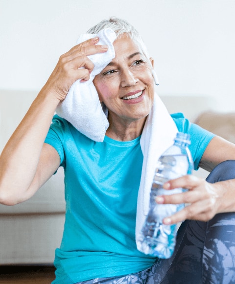 lder woman wiping sweat from her face after doing a workout at home