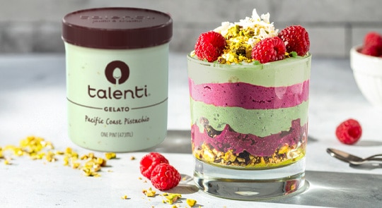An ube pistachio parfait with layers of ube halaya and pistachio gelato in a clear glass and fresh fruit and nuts 