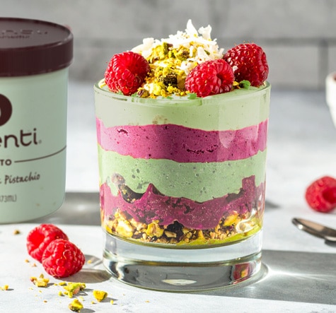 An ube pistachio parfait with layers of ube halaya and pistachio gelato in a clear glass and fresh fruit and nuts