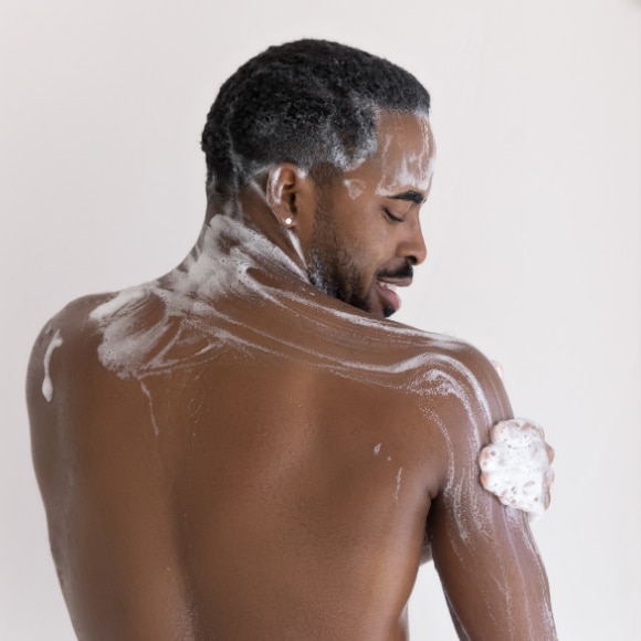 Young African American man exfoliating in the shower with Dove Men+Care body scrub 