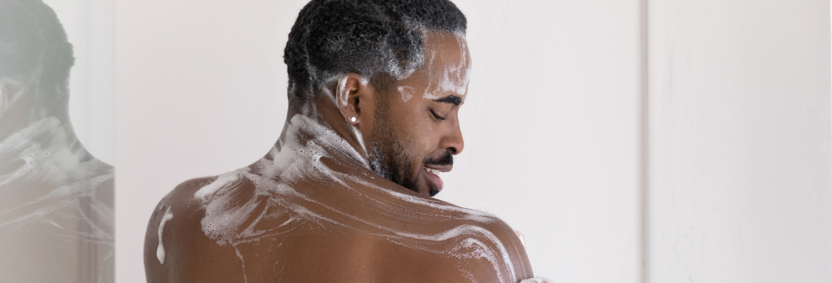 Young African American man exfoliating in the shower with Dove Men+Care body scrub