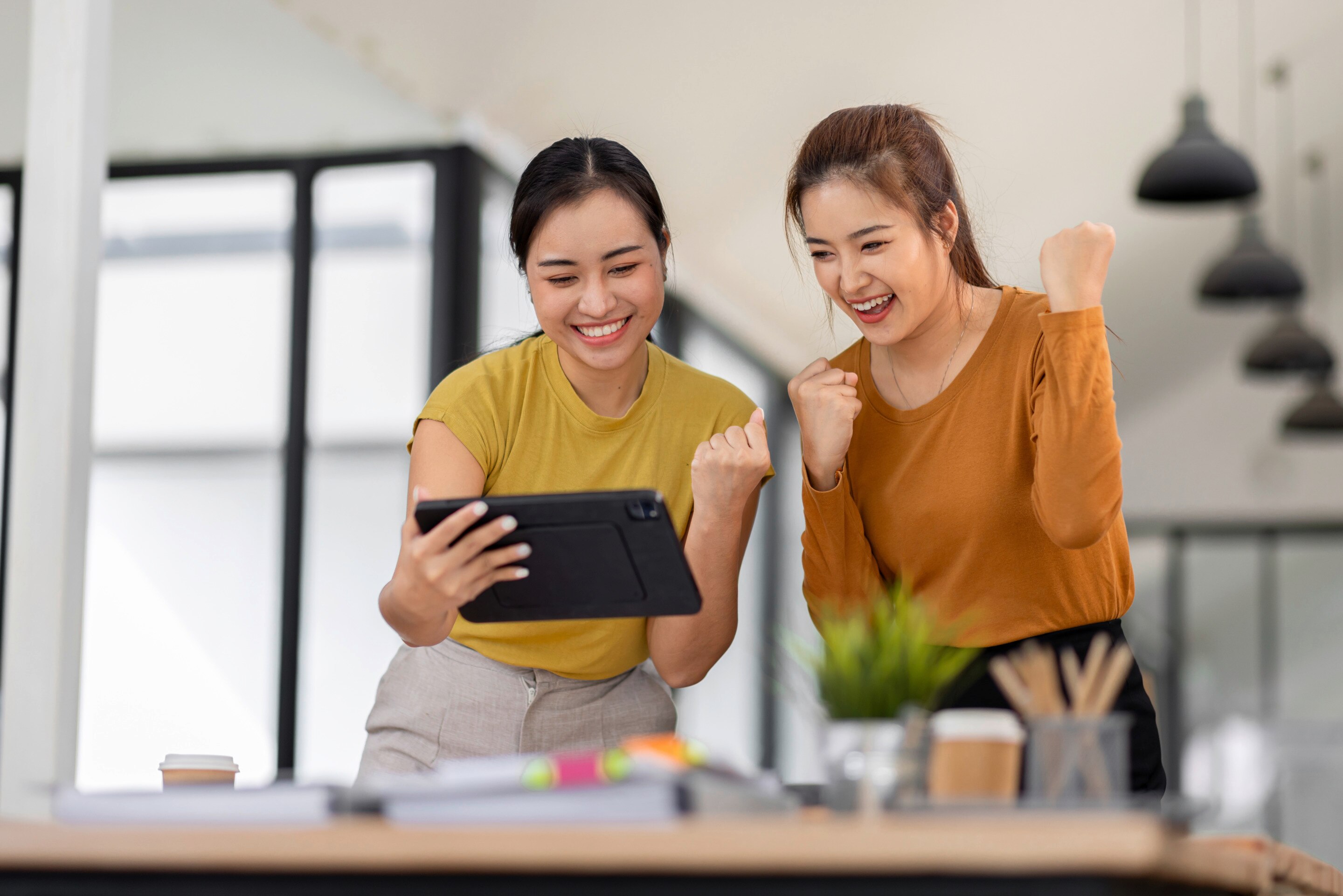 Two friends cheering while watching a video on tablet.