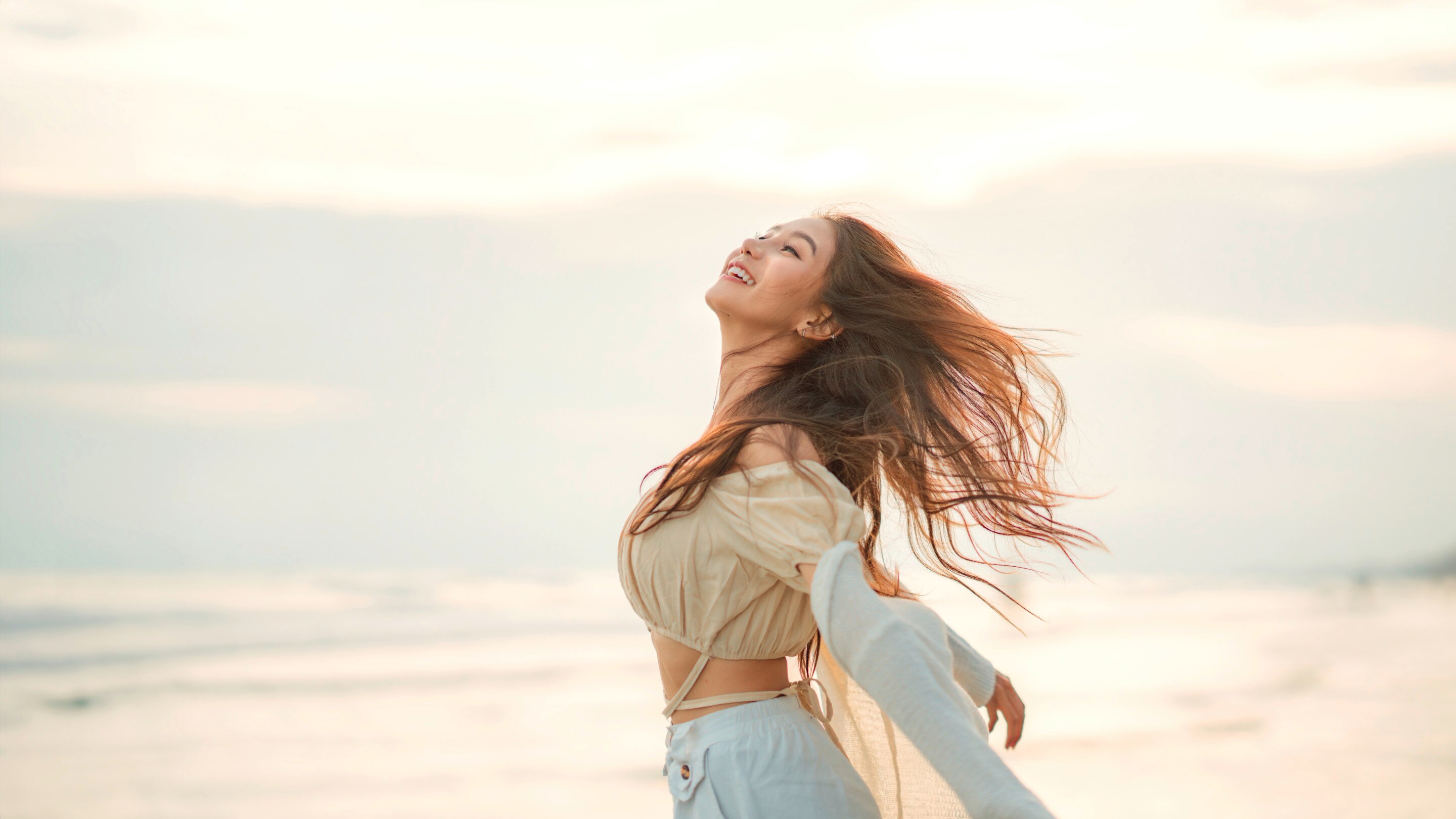 Asian woman with long brown hair feeling free at beach.