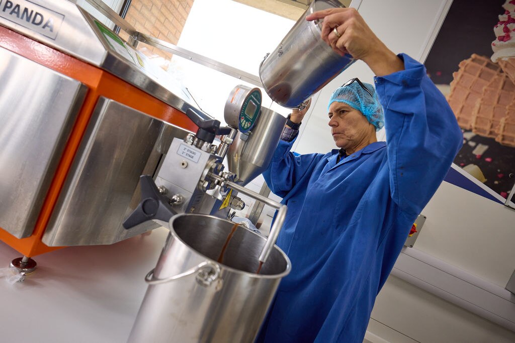 Person in protective uniform pouring liquid from a container into a large mixing machine