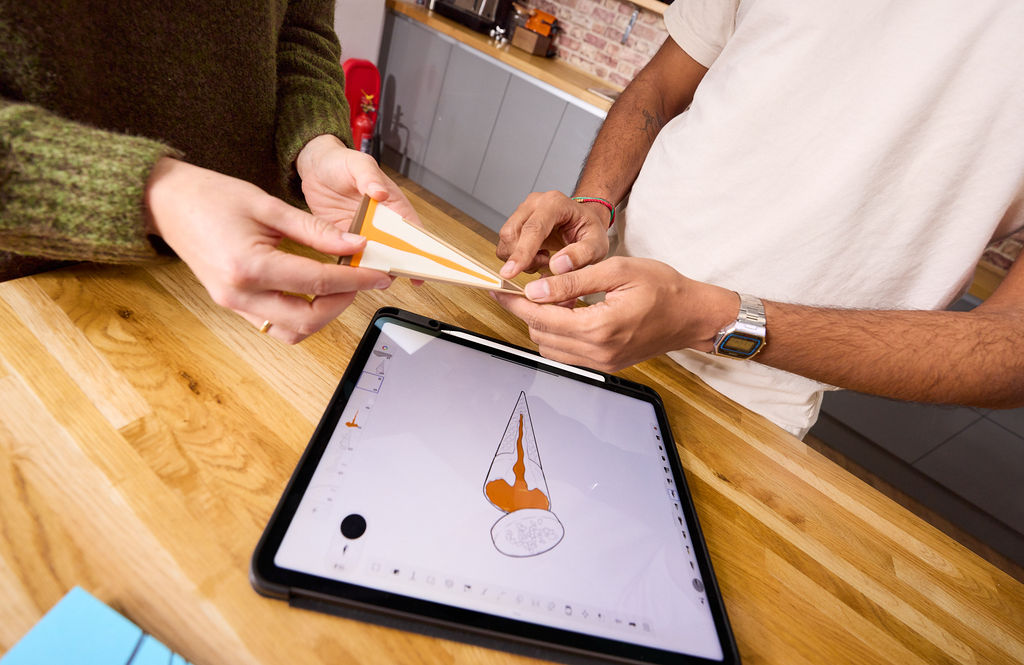 Two people handling a cone-shaped ice cream packaging prototype over a tablet