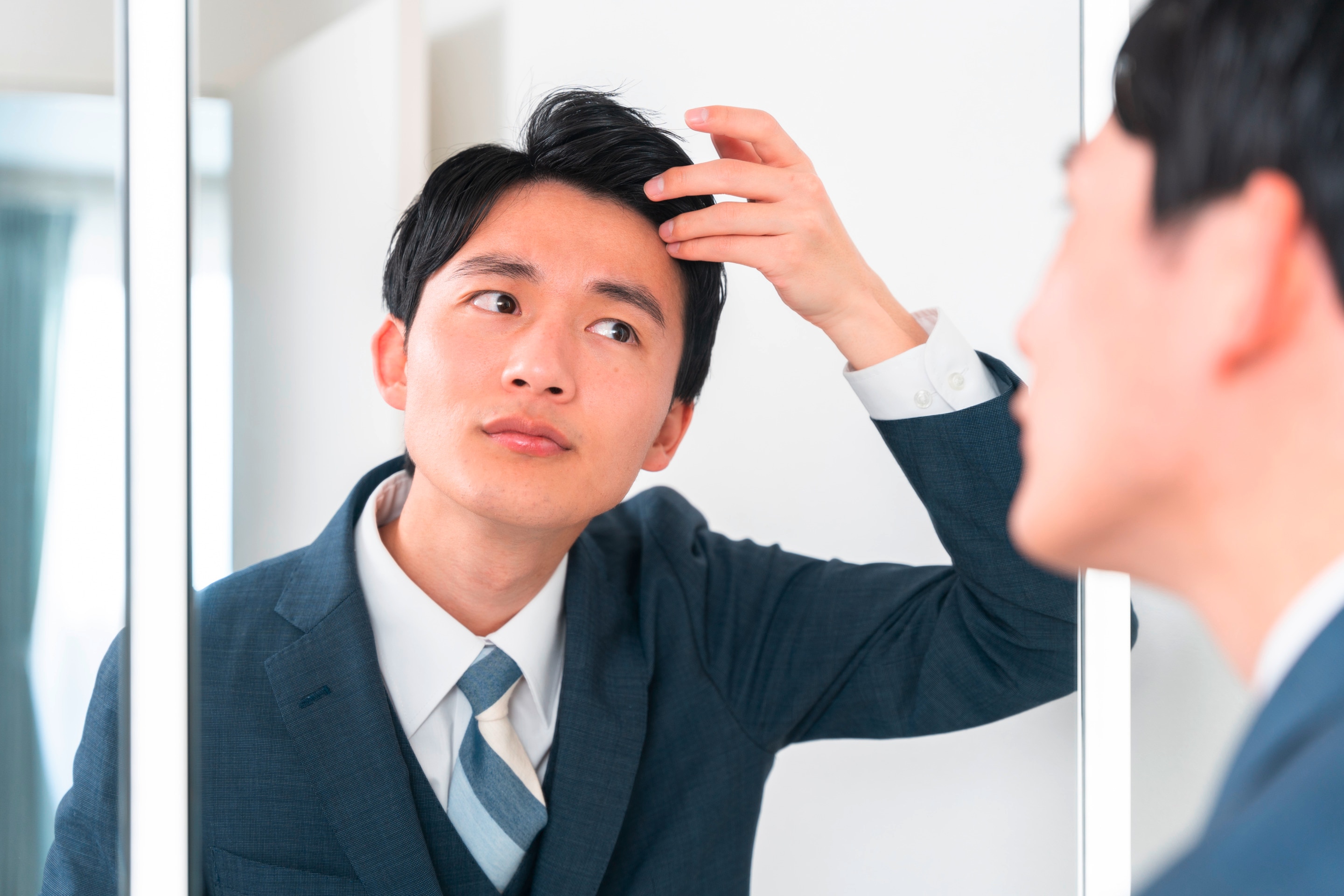Man checks his hair while looking at mirror.