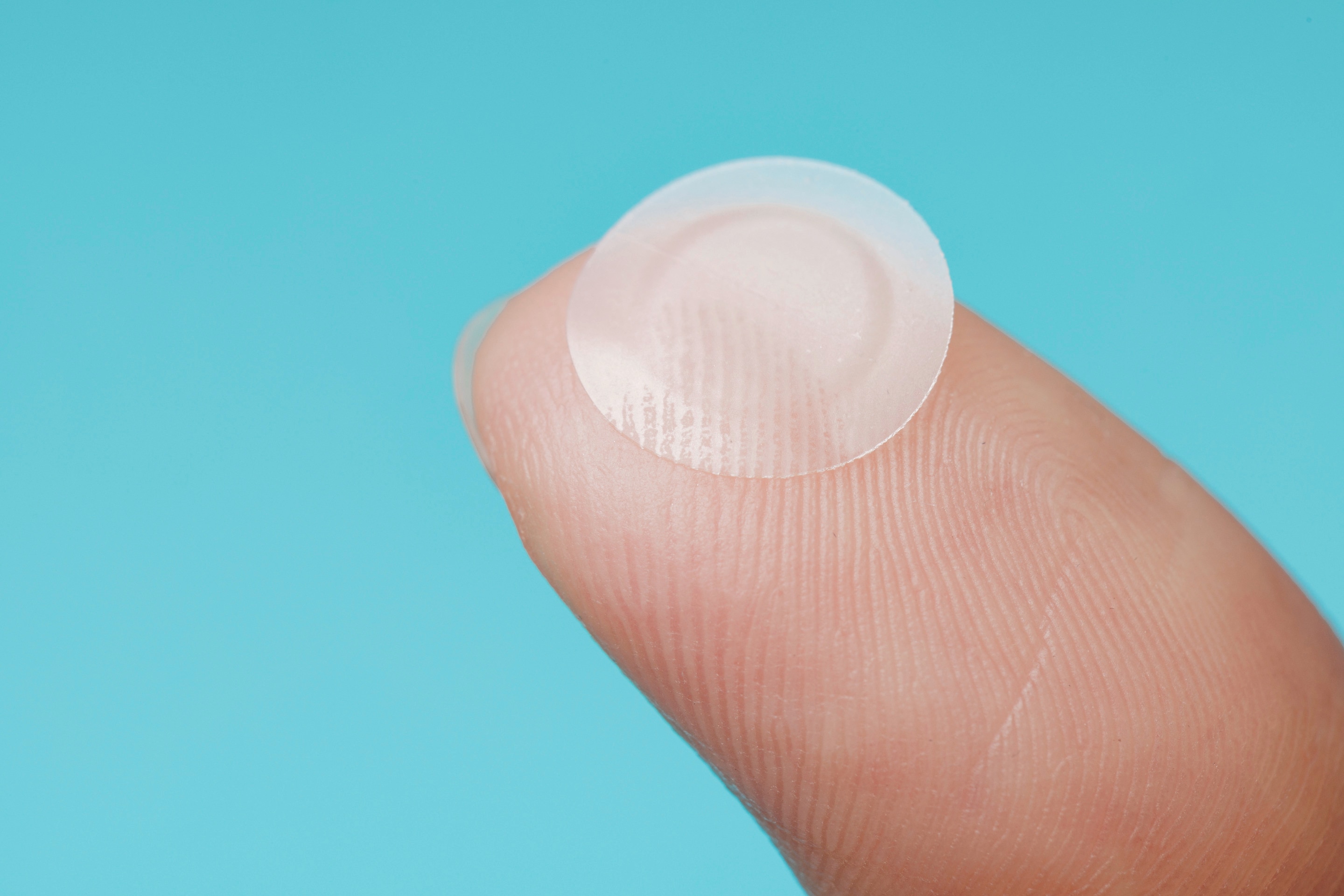 Closeup of finger holding up pimple patch.