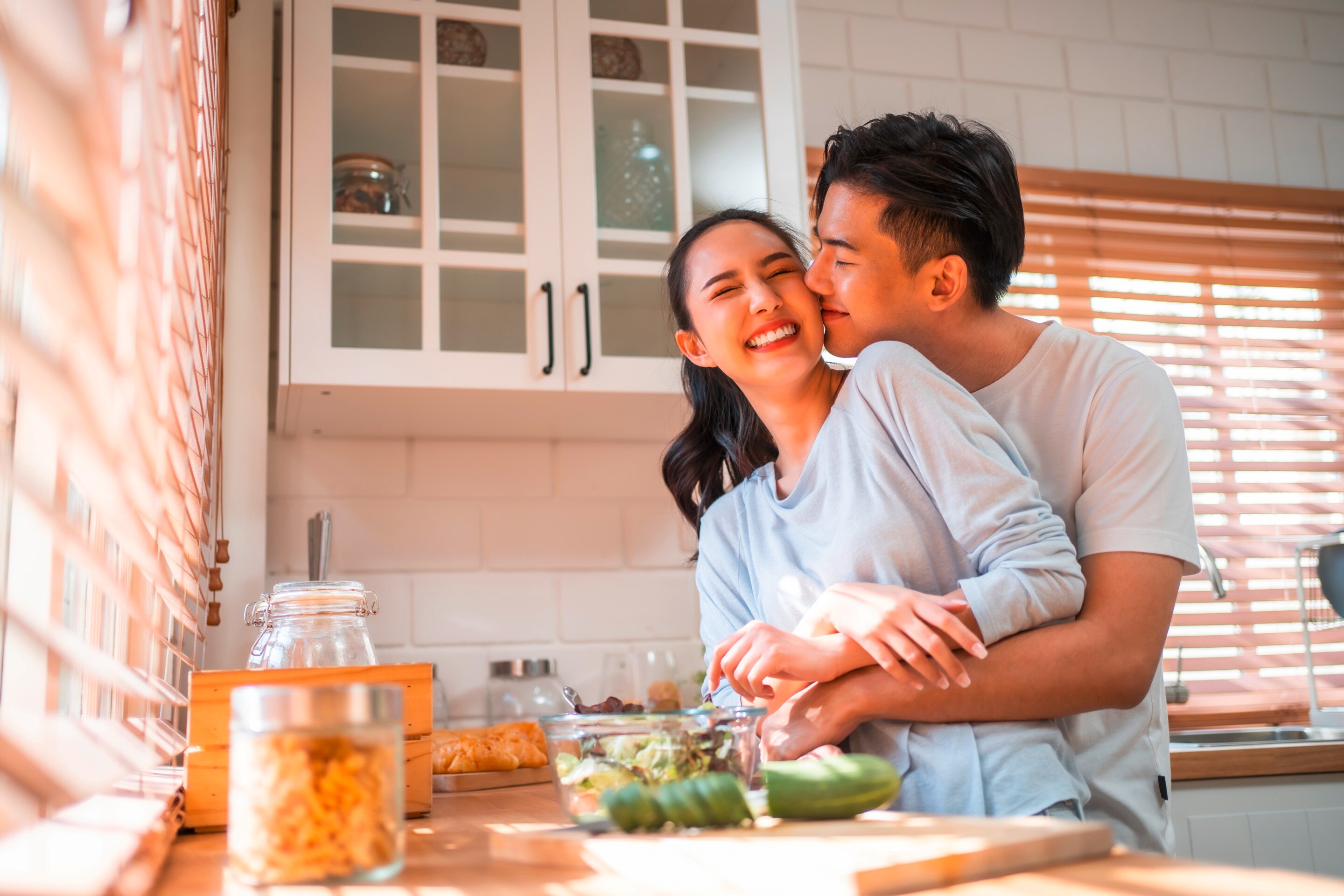 A happy couple share a hug while preparing a meal together in the kitchen.