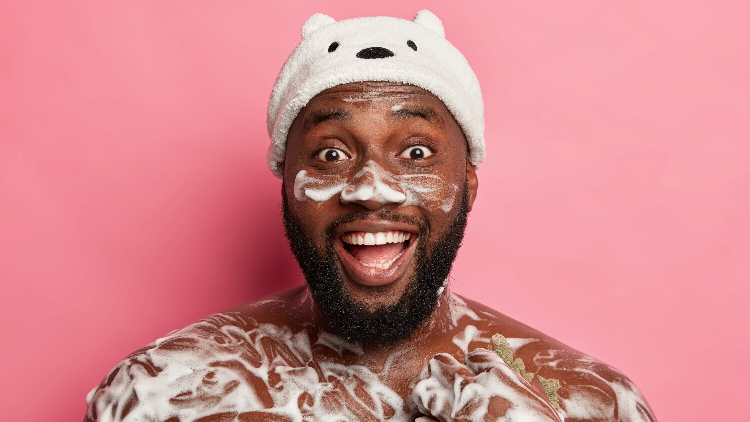 Happy man with lathered body wash on his skin while using a shower loofah