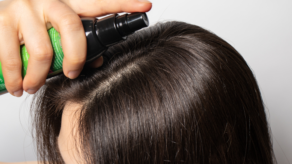 Woman applying hair tonic to scalp for hair growth