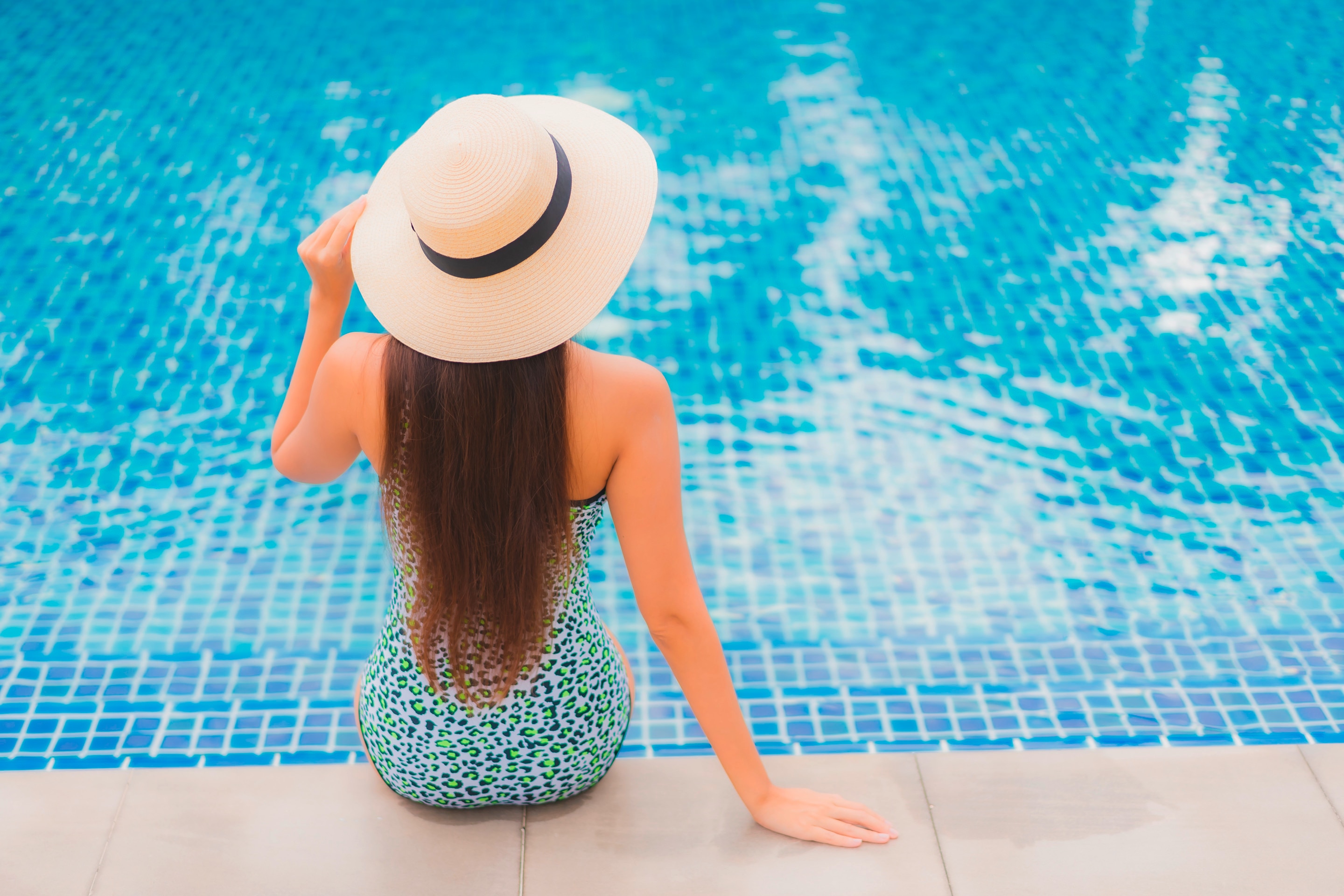 A woman wearing a hat sitting at the edge of a swimming pool.