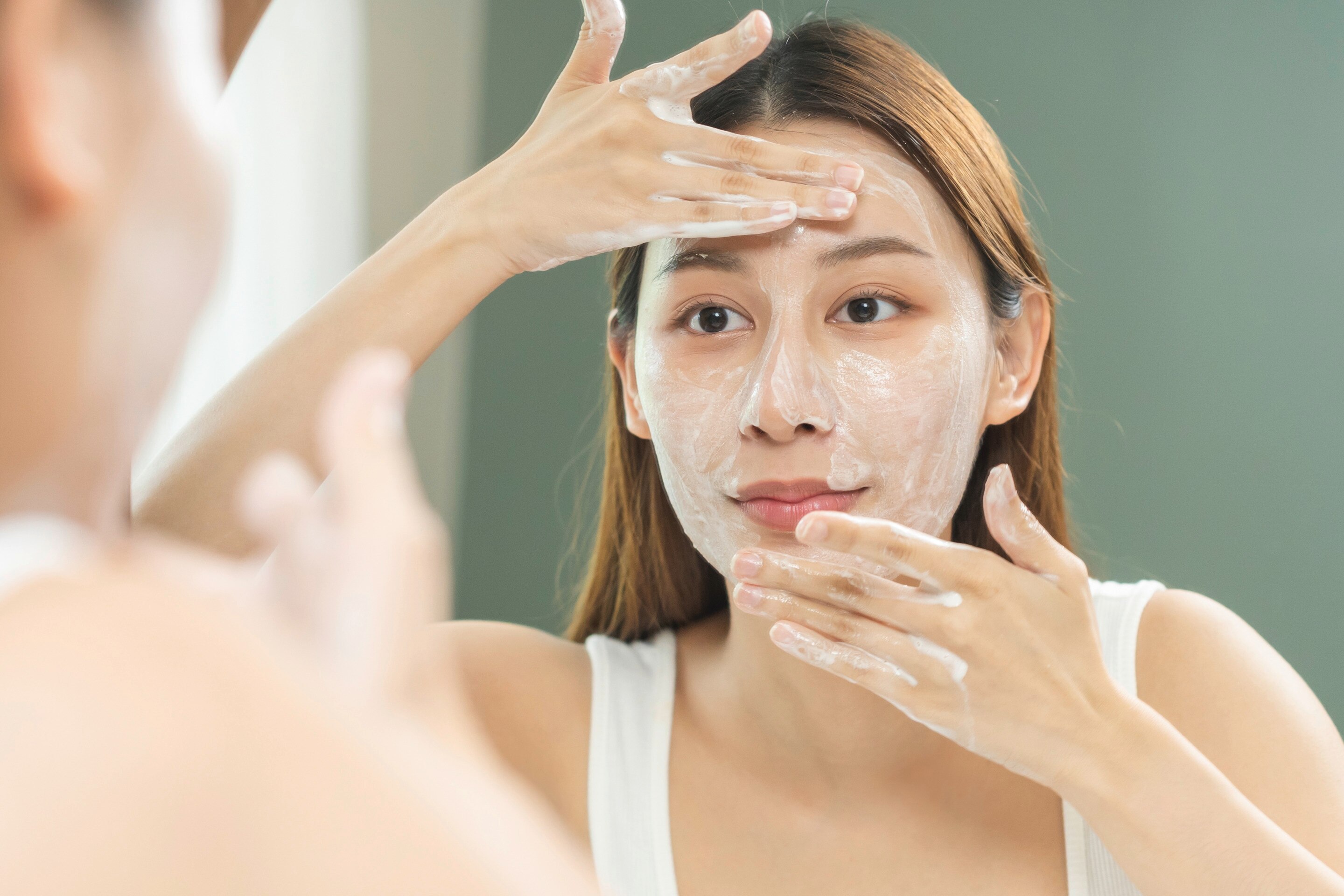 Woman looking at herself in the mirror while putting product on her face. 